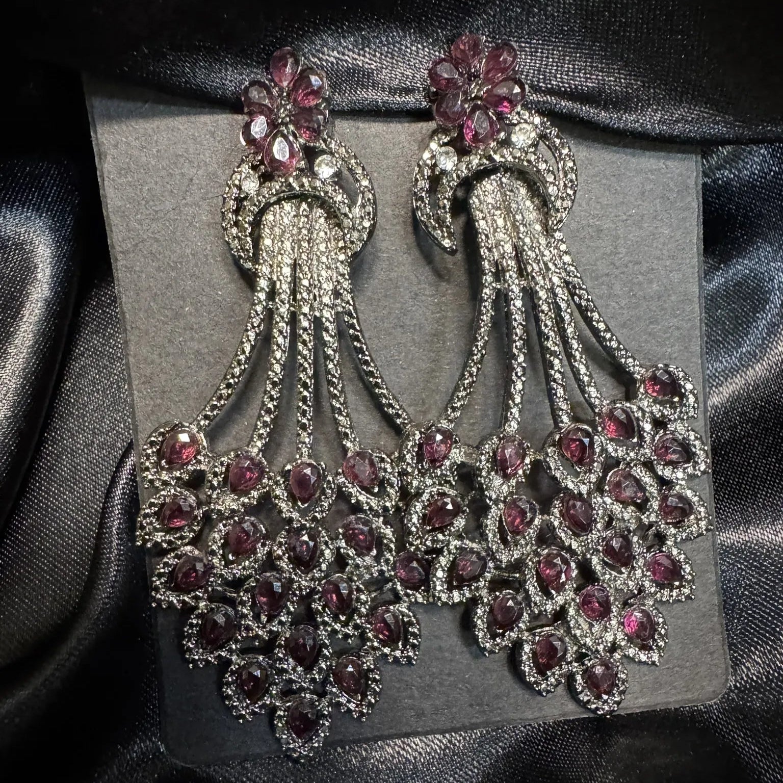 Pair of ornate earrings with hotpink gemstones on a dark background