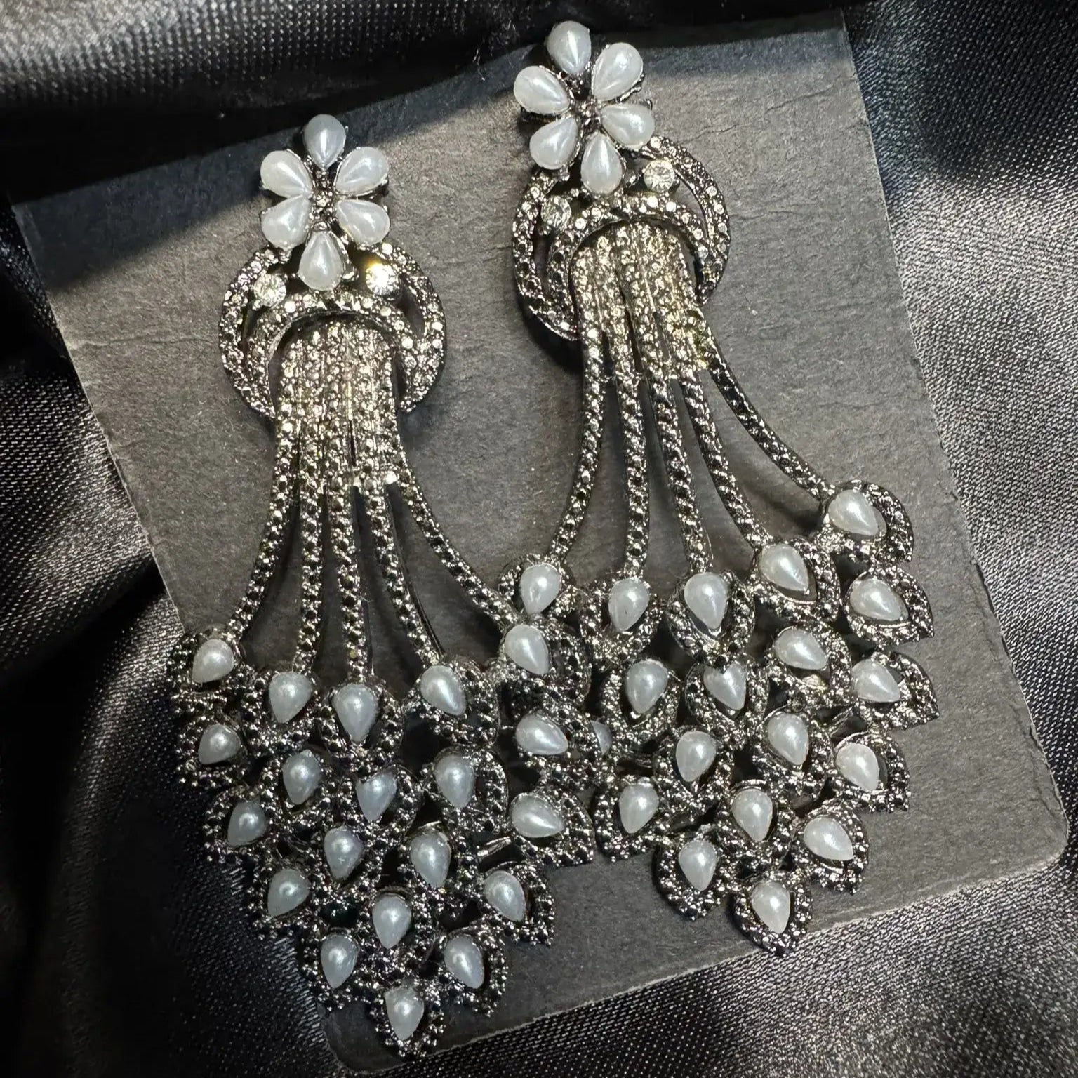 Pair of ornate earrings with grey gemstones on a dark fabric background