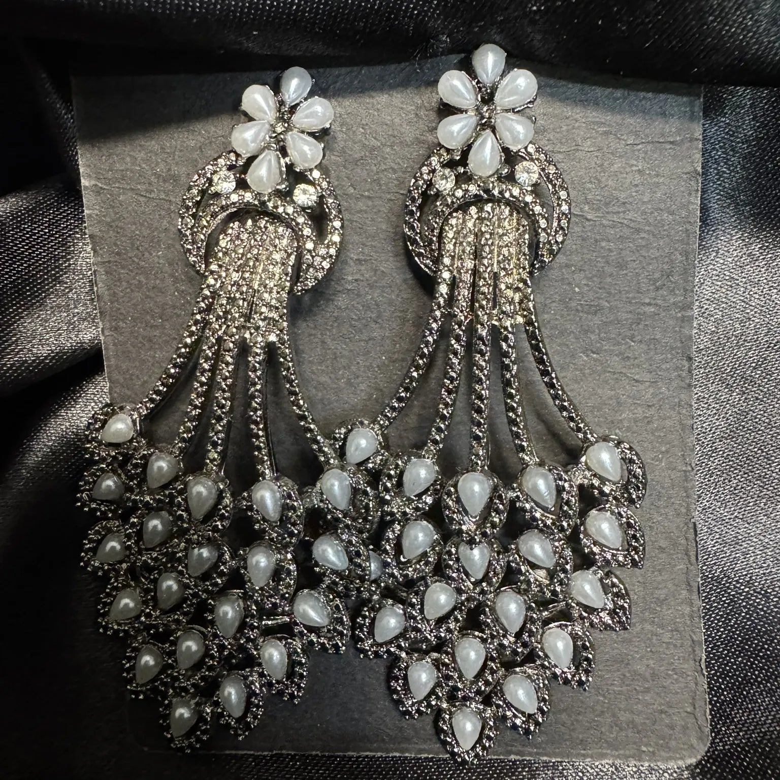 Pair of ornate earrings with grey pearl-like stones on a black satin background