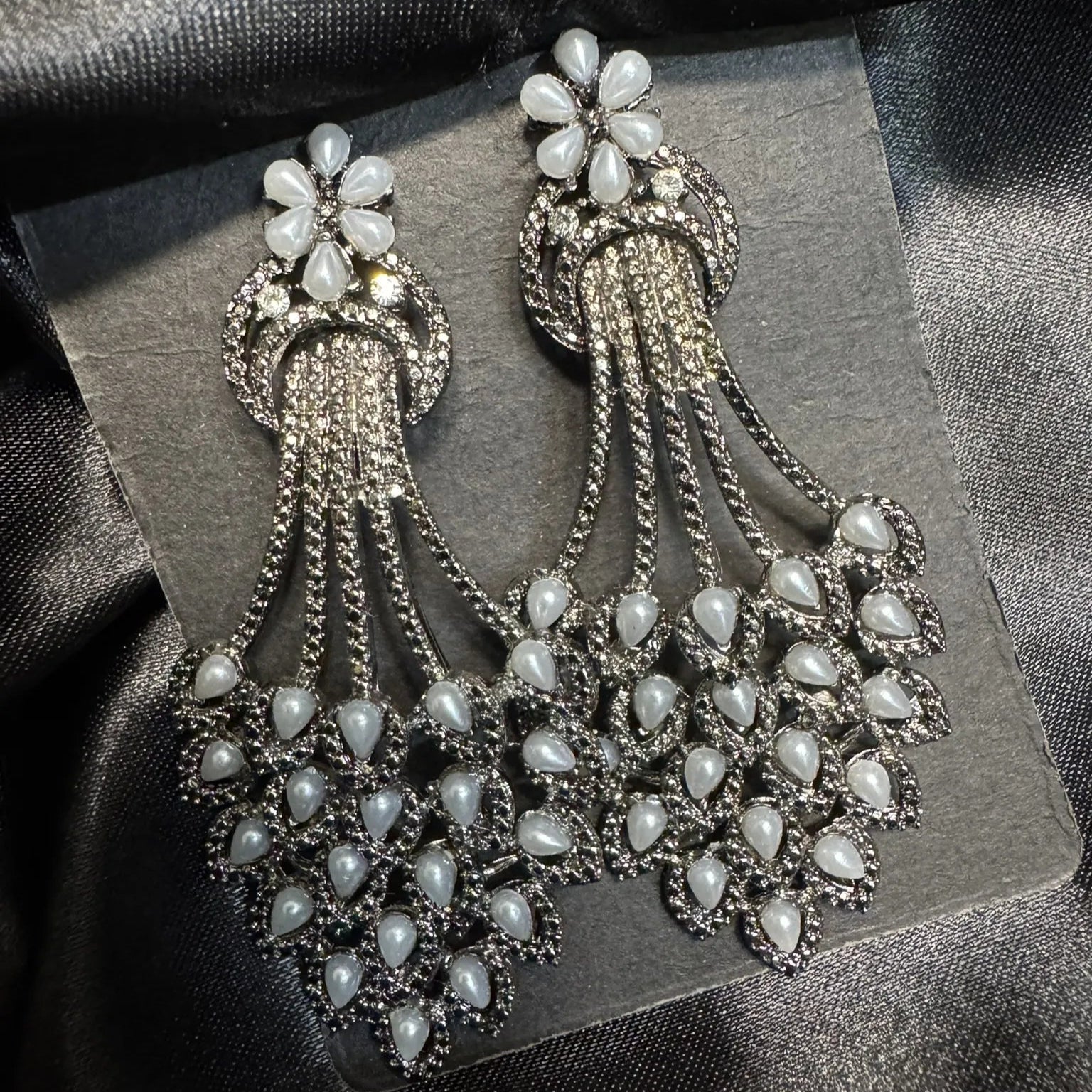 Pair of ornate earrings with grey pearl-like stones on a dark fabric background