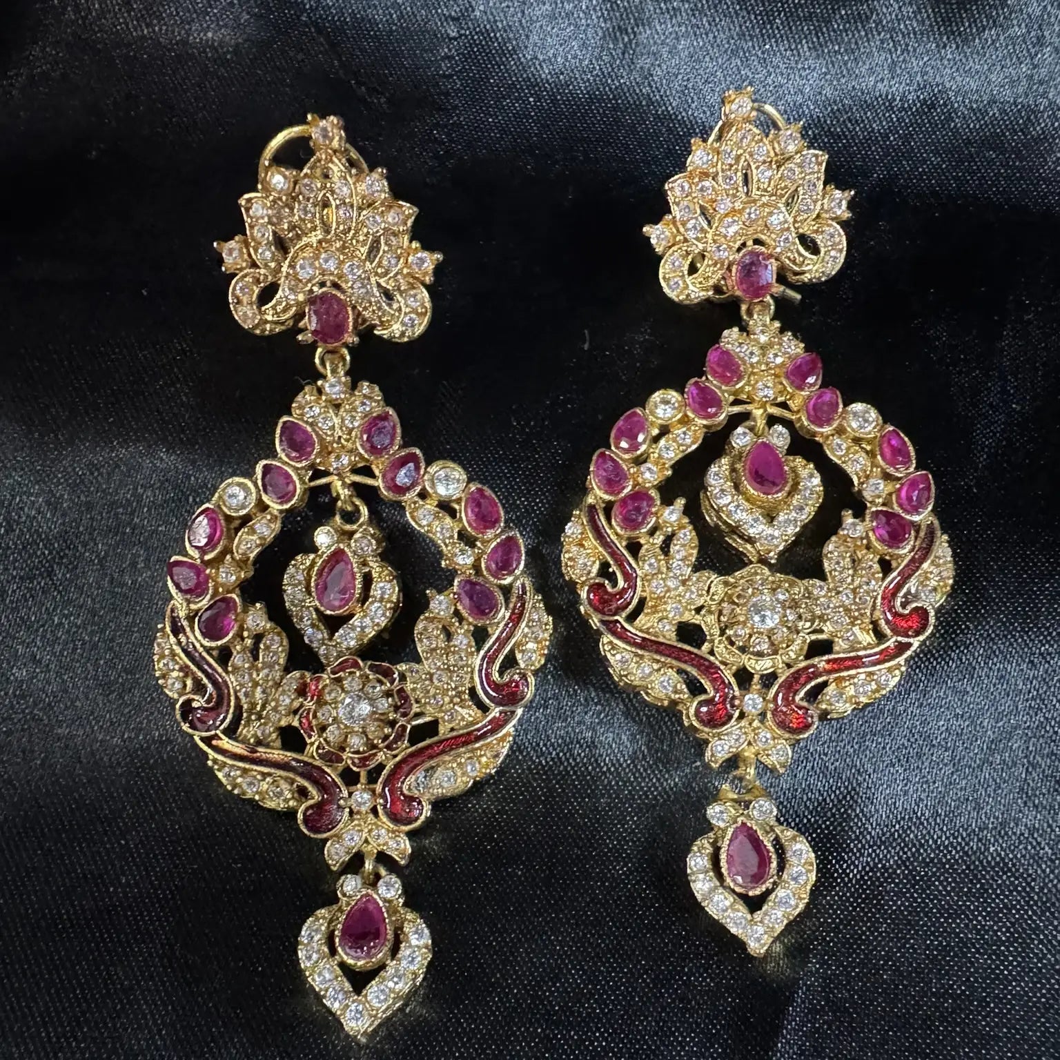 Pair of ornate gold plated earrings with red gemstones on a dark fabric background