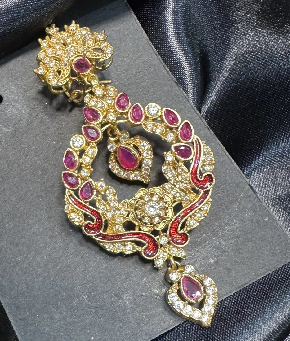 Ornate gold and red earrings on a black card against a dark fabric background