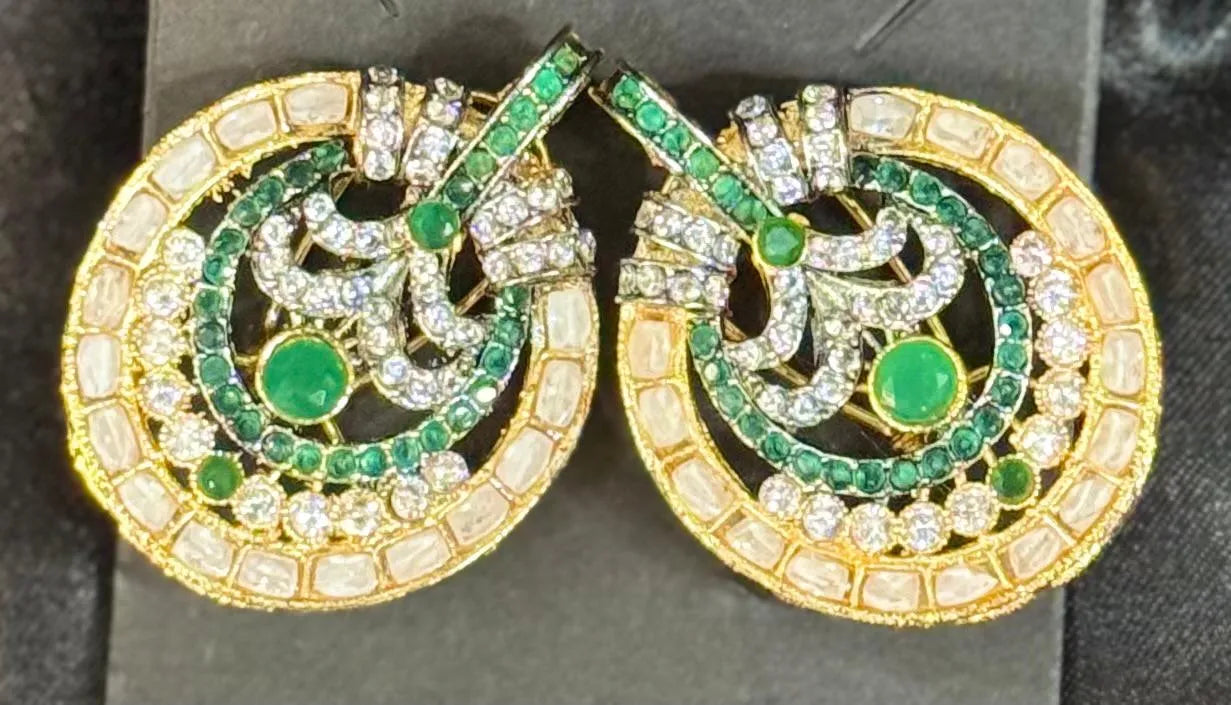 Pair of gold plated earrings with green and clear gemstones on a dark background
