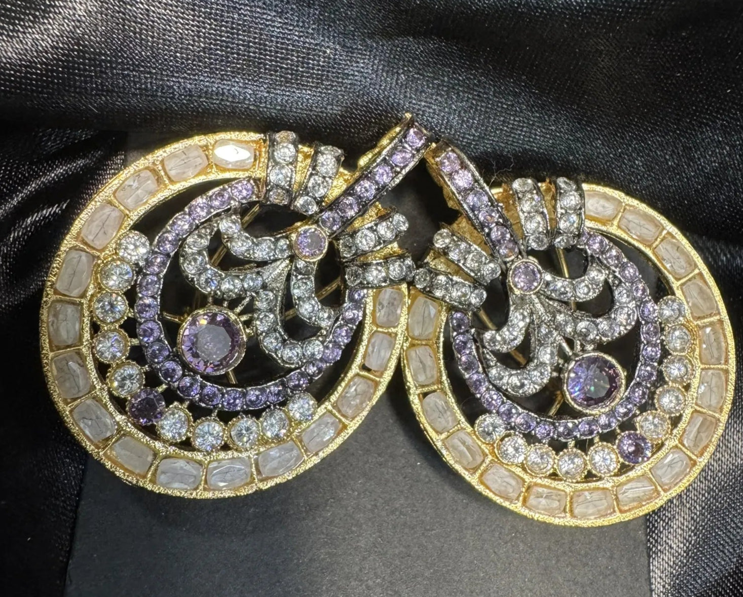 Pair of ornate earrings with purple gemstones on a black satin background