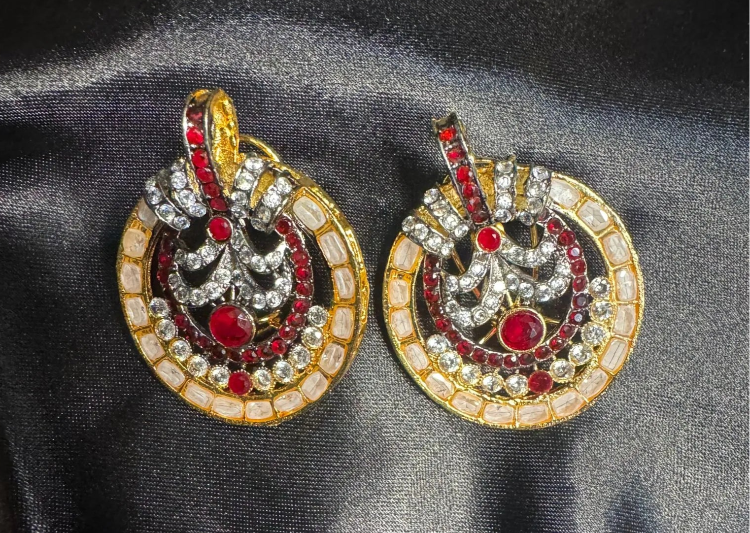Pair of ornate earrings with red and clear gemstones on a black satin background