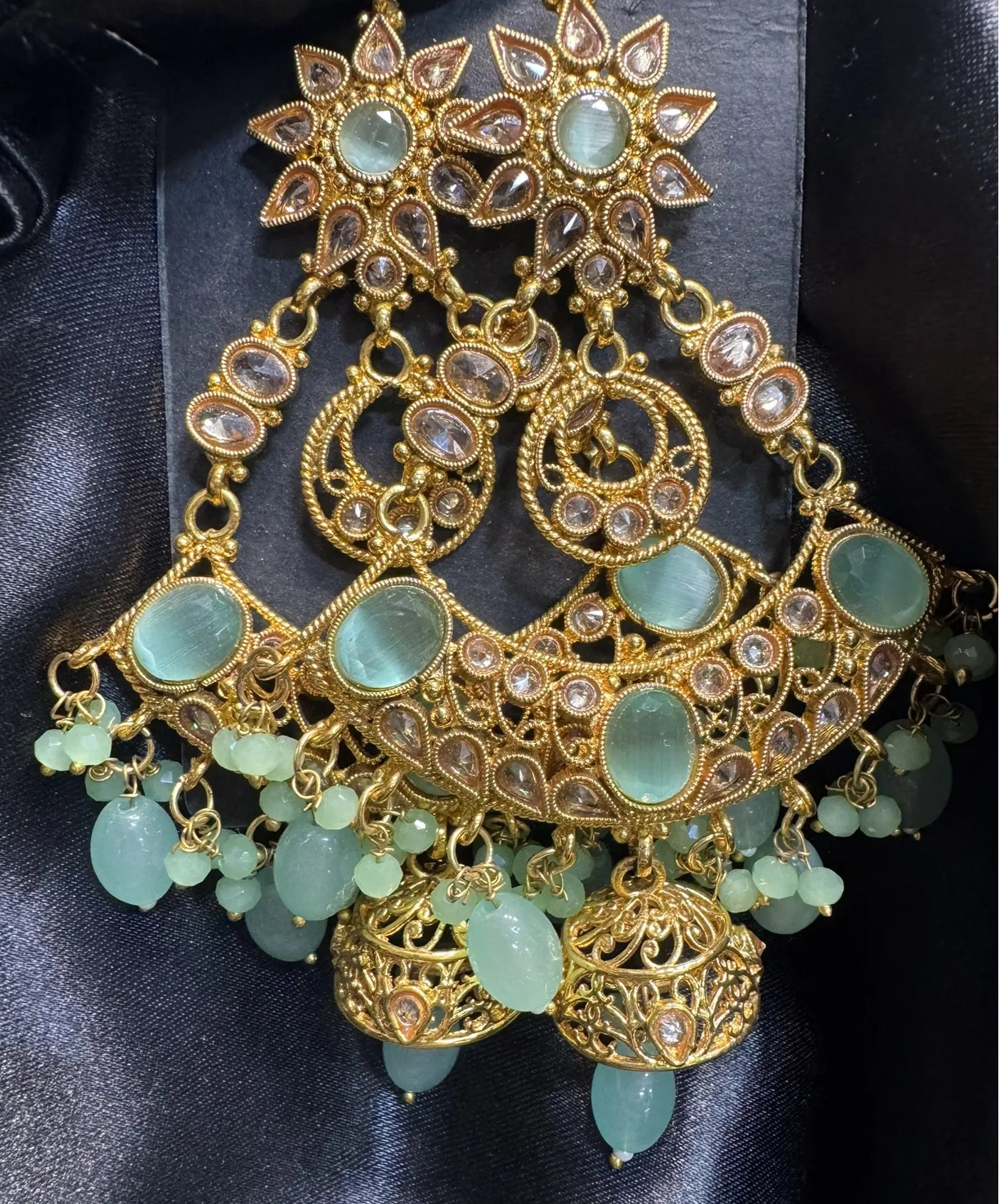 Ornate gold and teal gemstone earrings on a black satin background