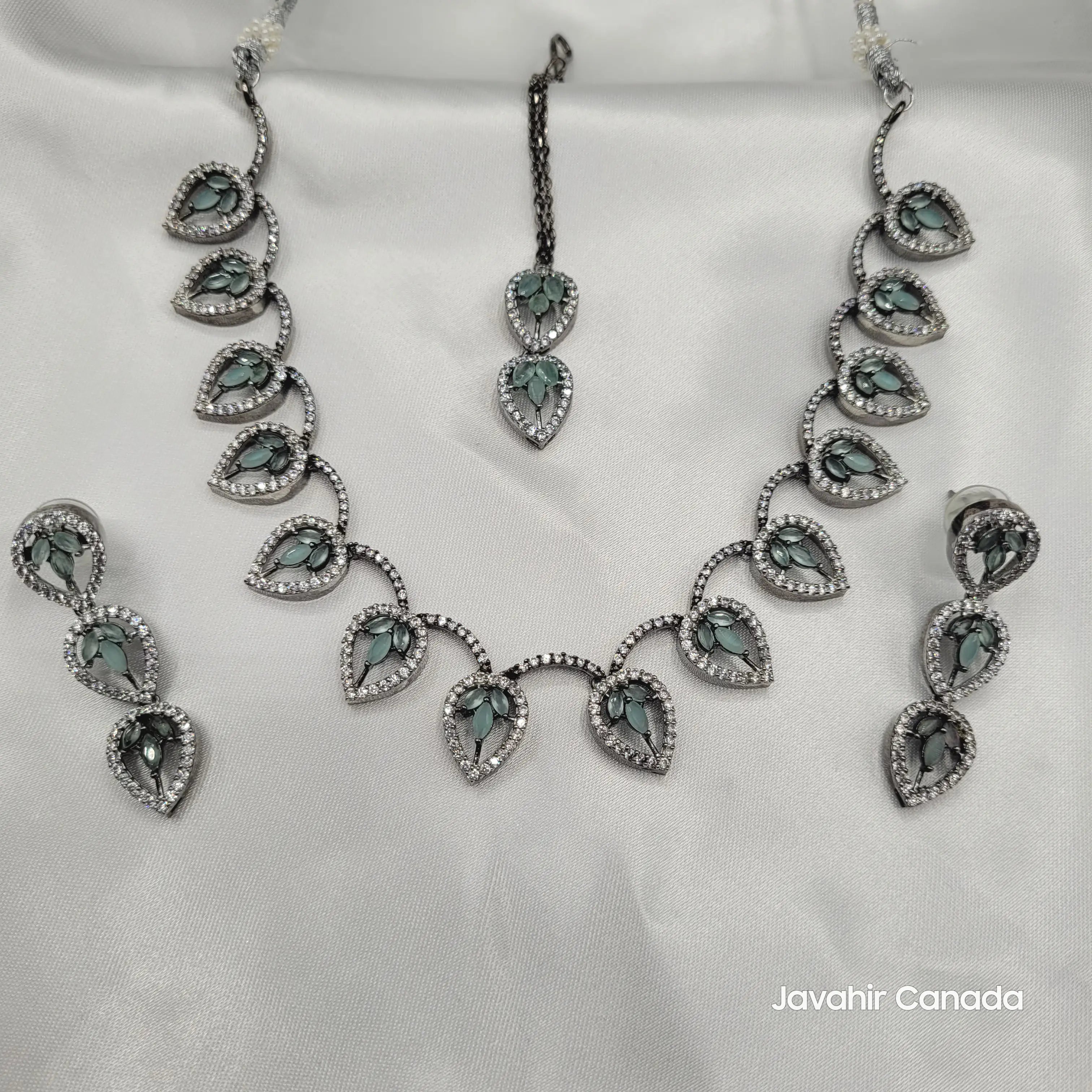 Top-down view of the complete JV08 necklace, earrings, and tika set on a satin background