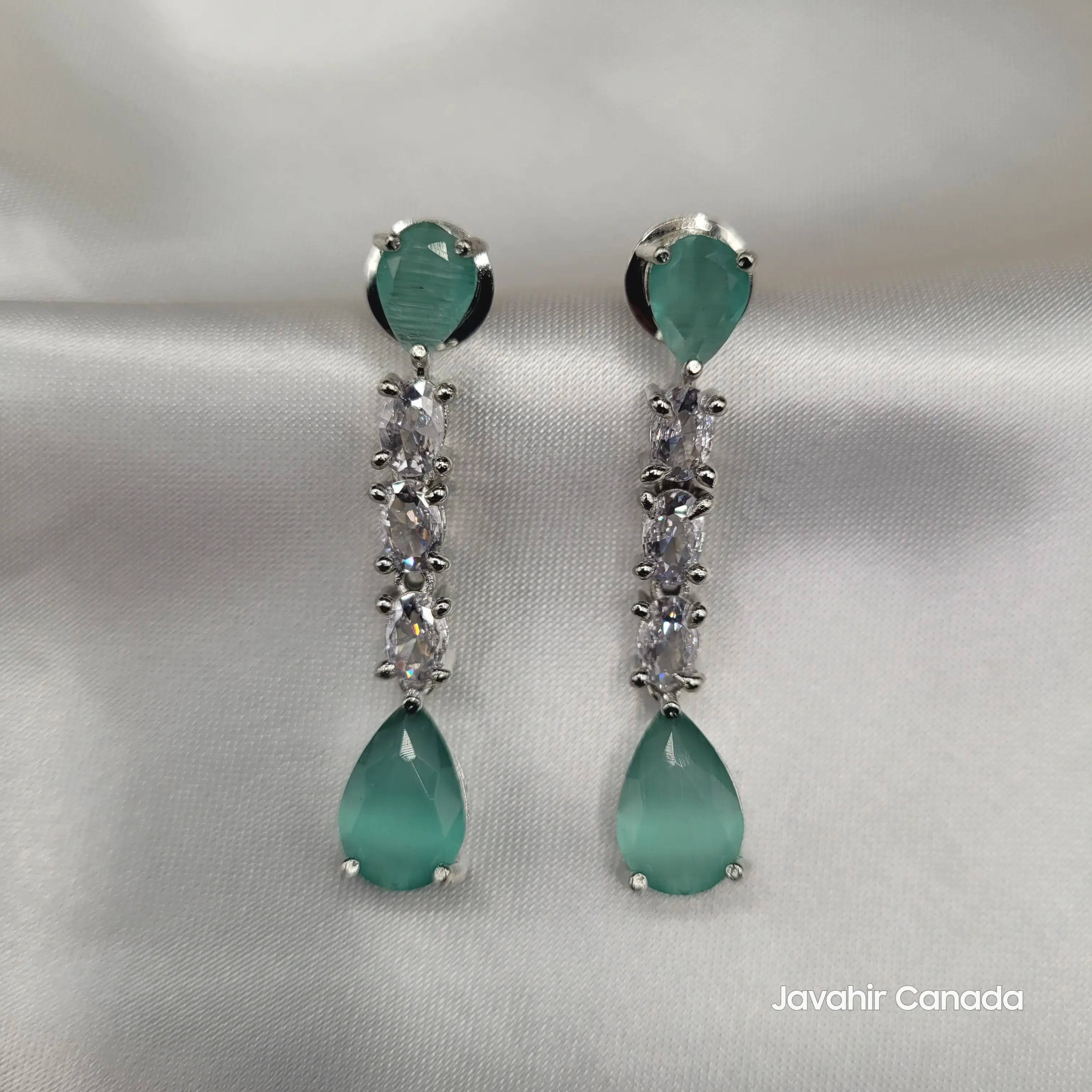Close-up of JV145 mint green teardrop earrings with American diamond accents on white satin background.