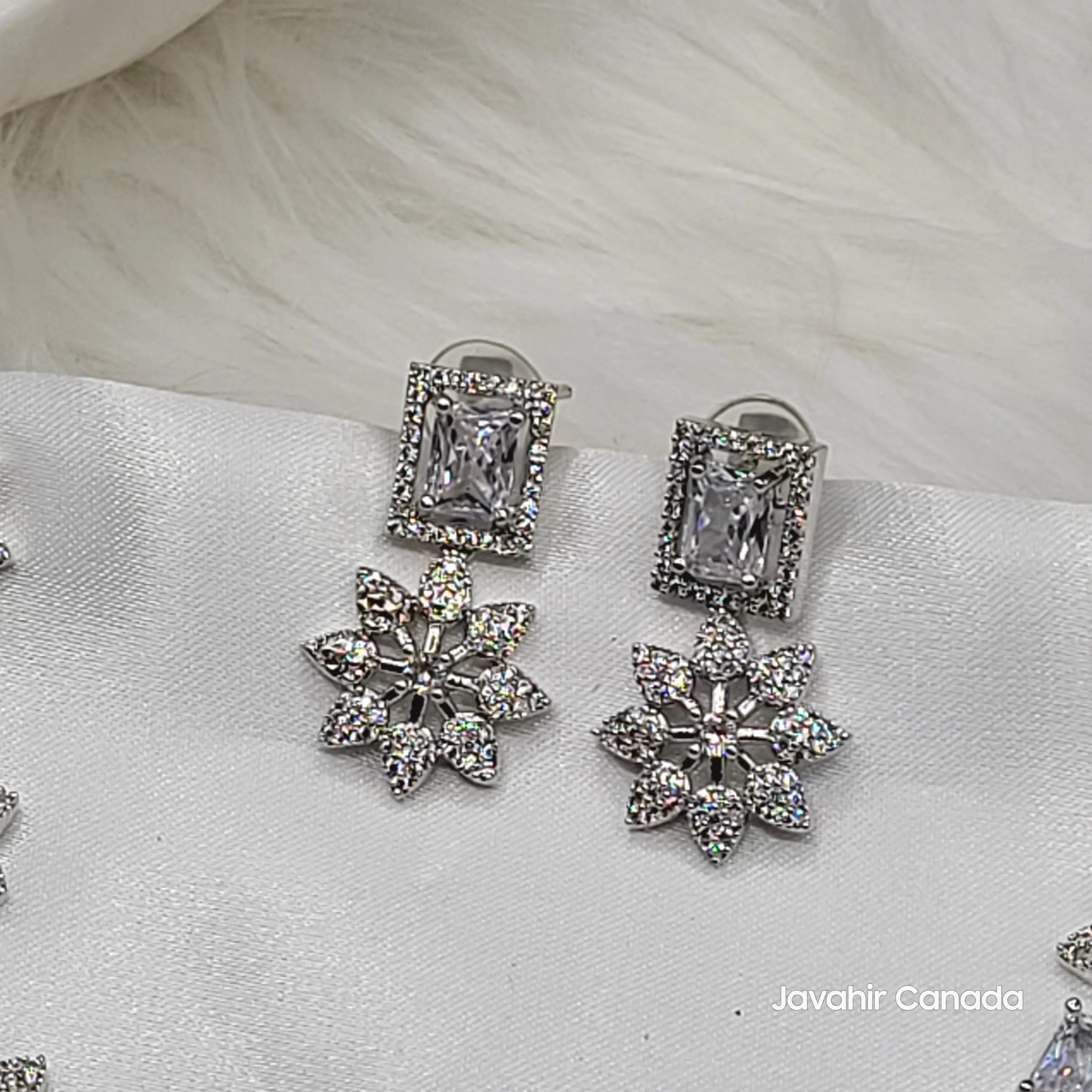 Pair of silver earrings with floral and rectangular designs on a white fabric background.