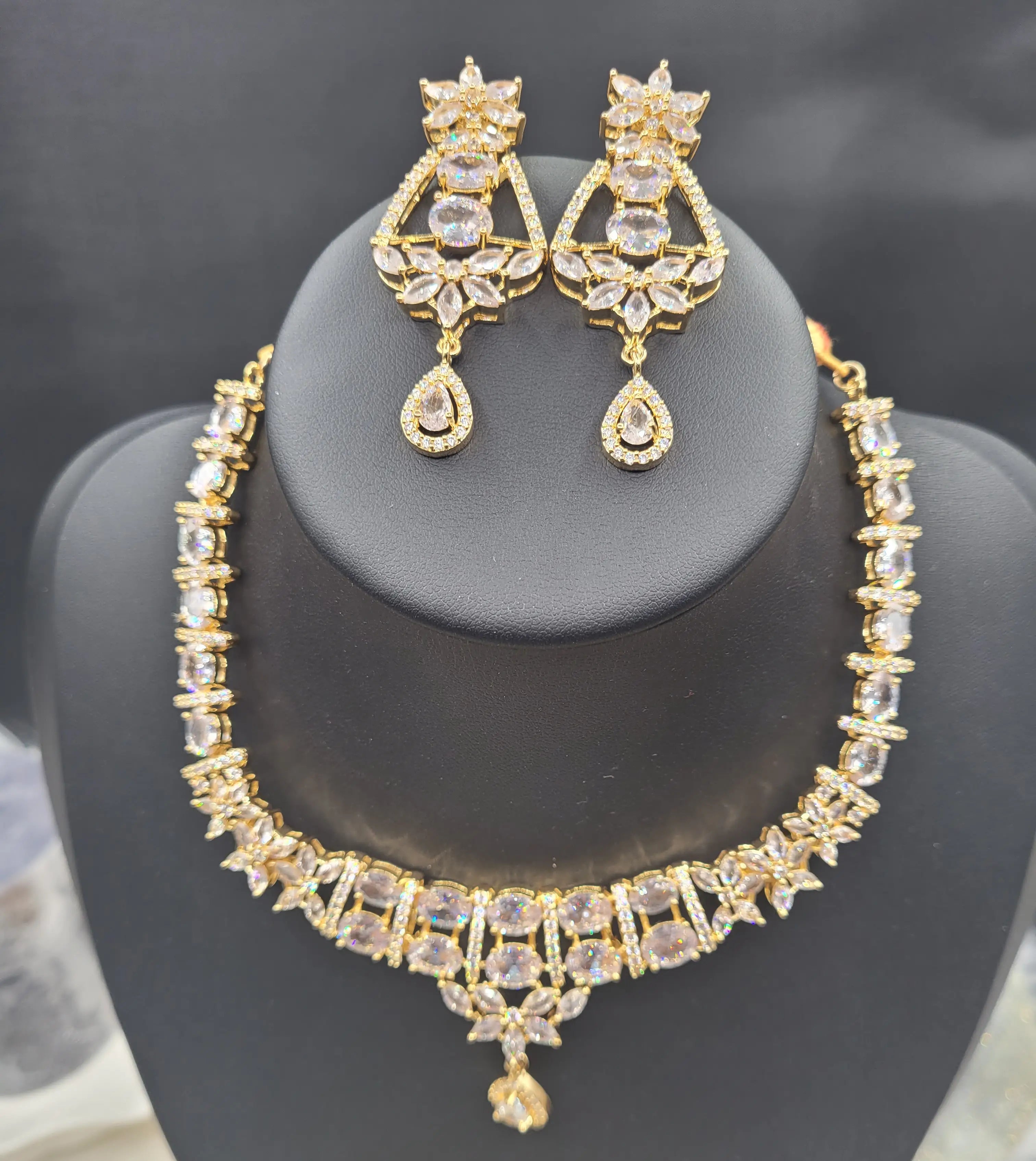Full JV150 necklace set in gold with clear stones and floral detailing on black stand.