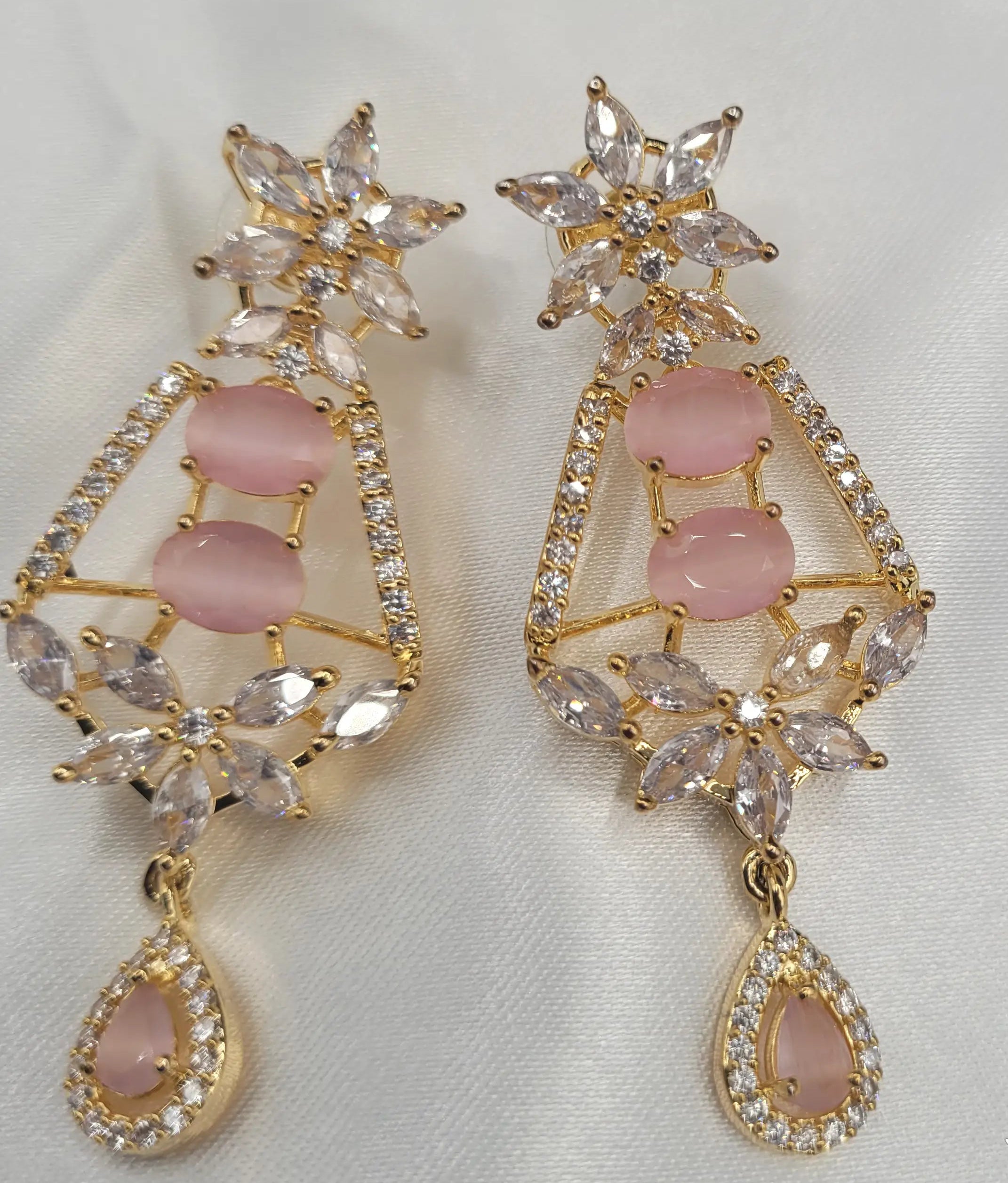 Close-up of JV150 earrings in gold with pink CZ stones and floral top on satin fabric.