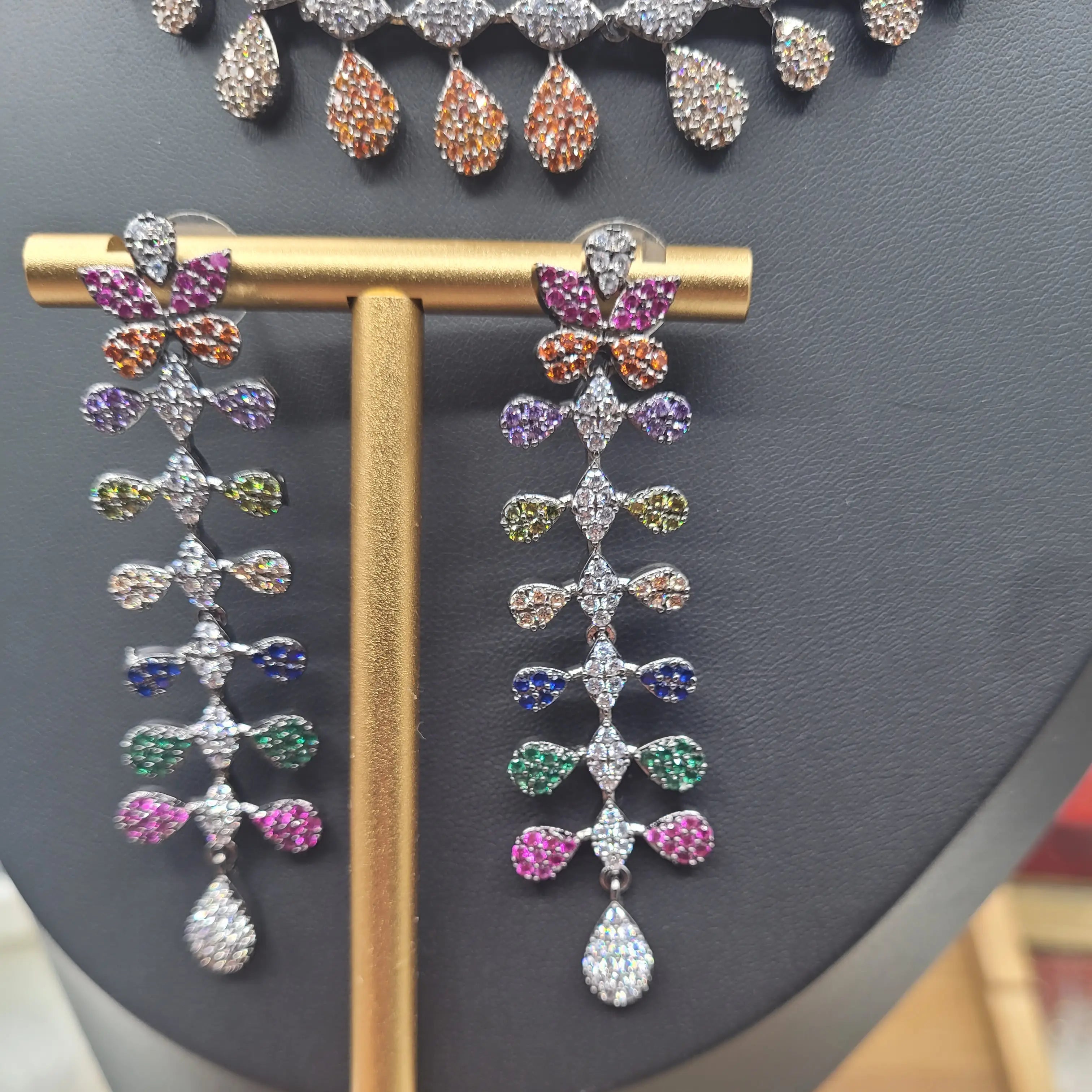 Multicolour zircon earrings from JV152 displayed on a gold T-bar stand, featuring floral and teardrop motifs in a cascading design.