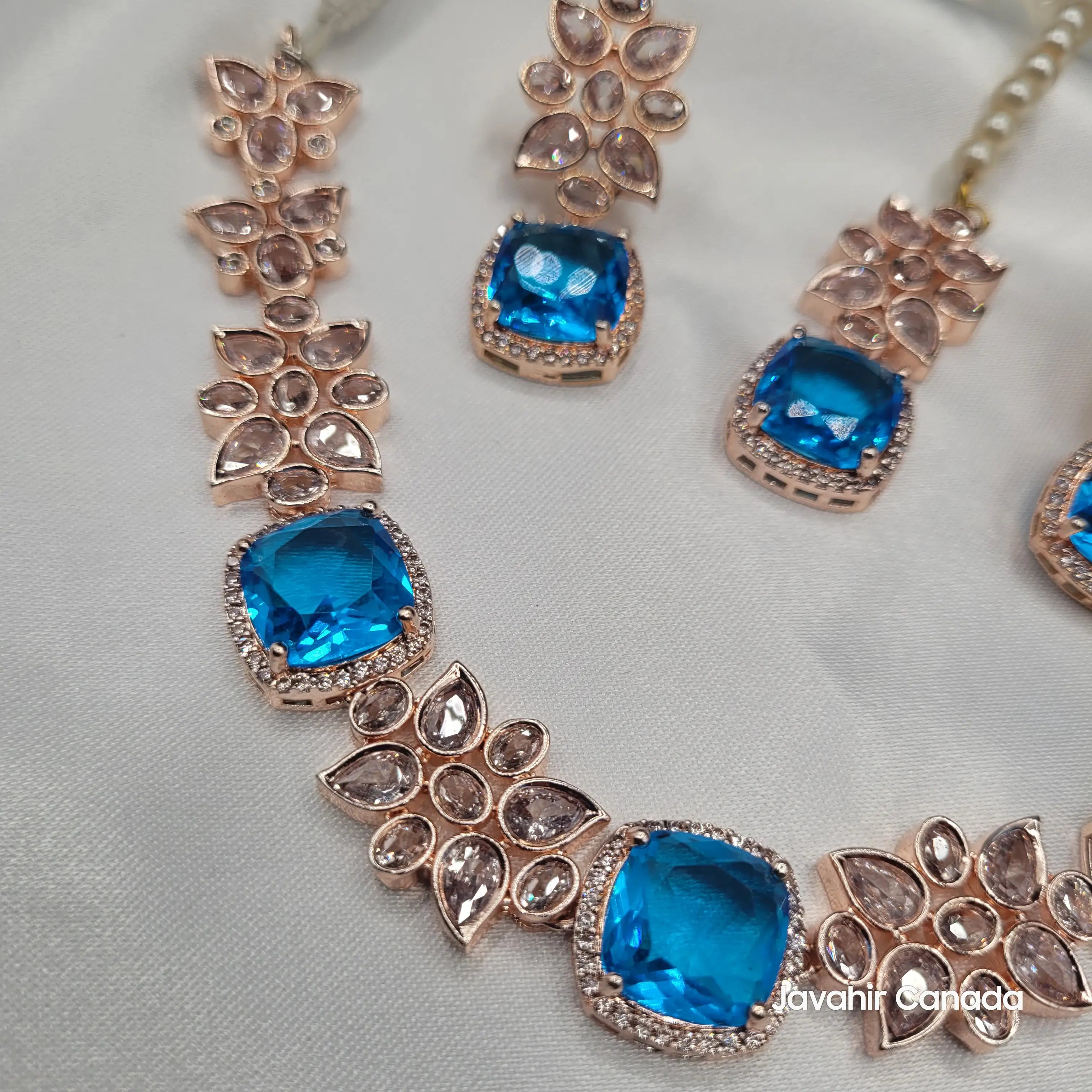 Side angle view of the JV153 necklace set with vivid blue zircon cushion-cut stones, surrounded by American diamonds in a rose gold frame.
