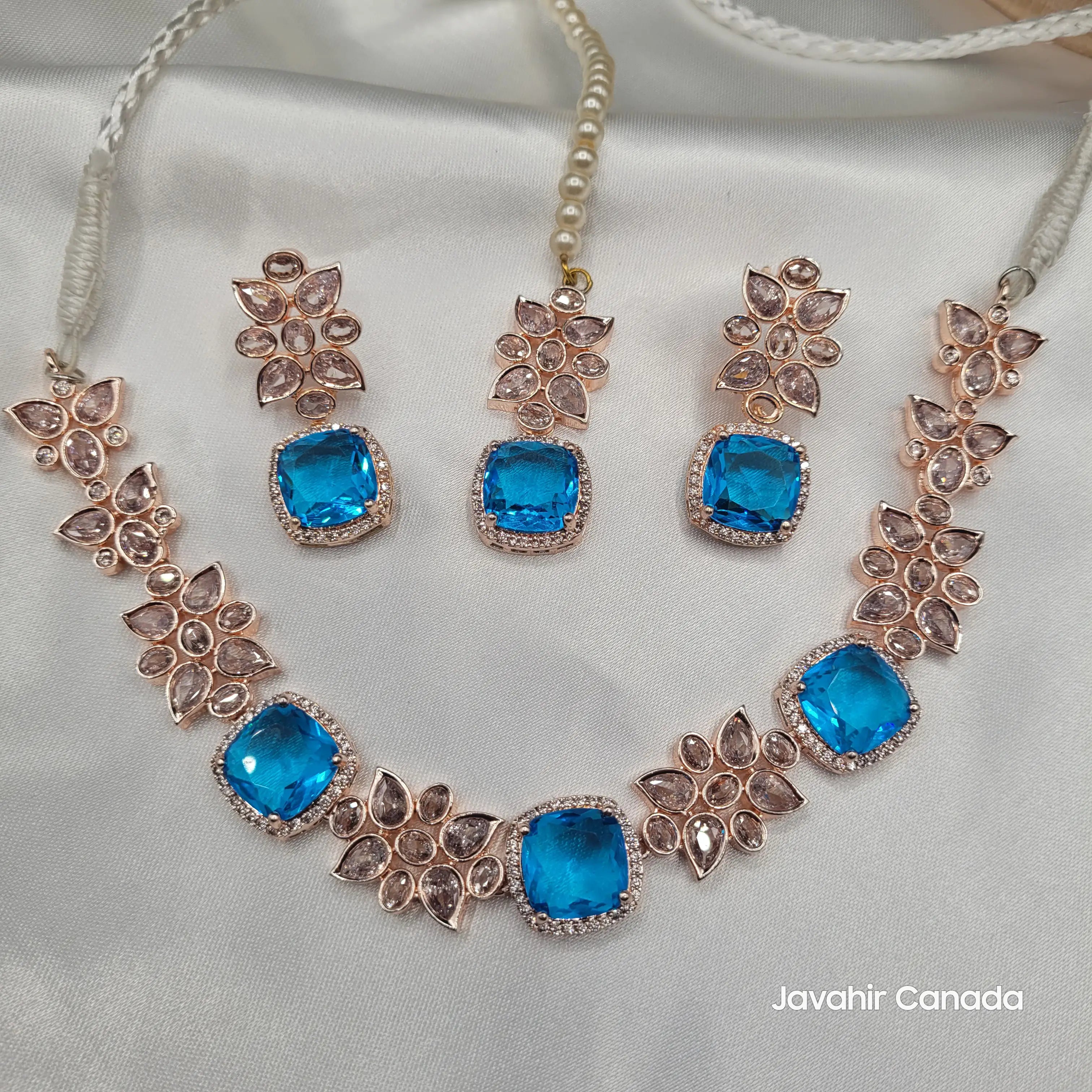 Complete blue zircon necklace set JV153 with matching earrings and tikka, featuring floral CZ work and pearl string on a white silk background.