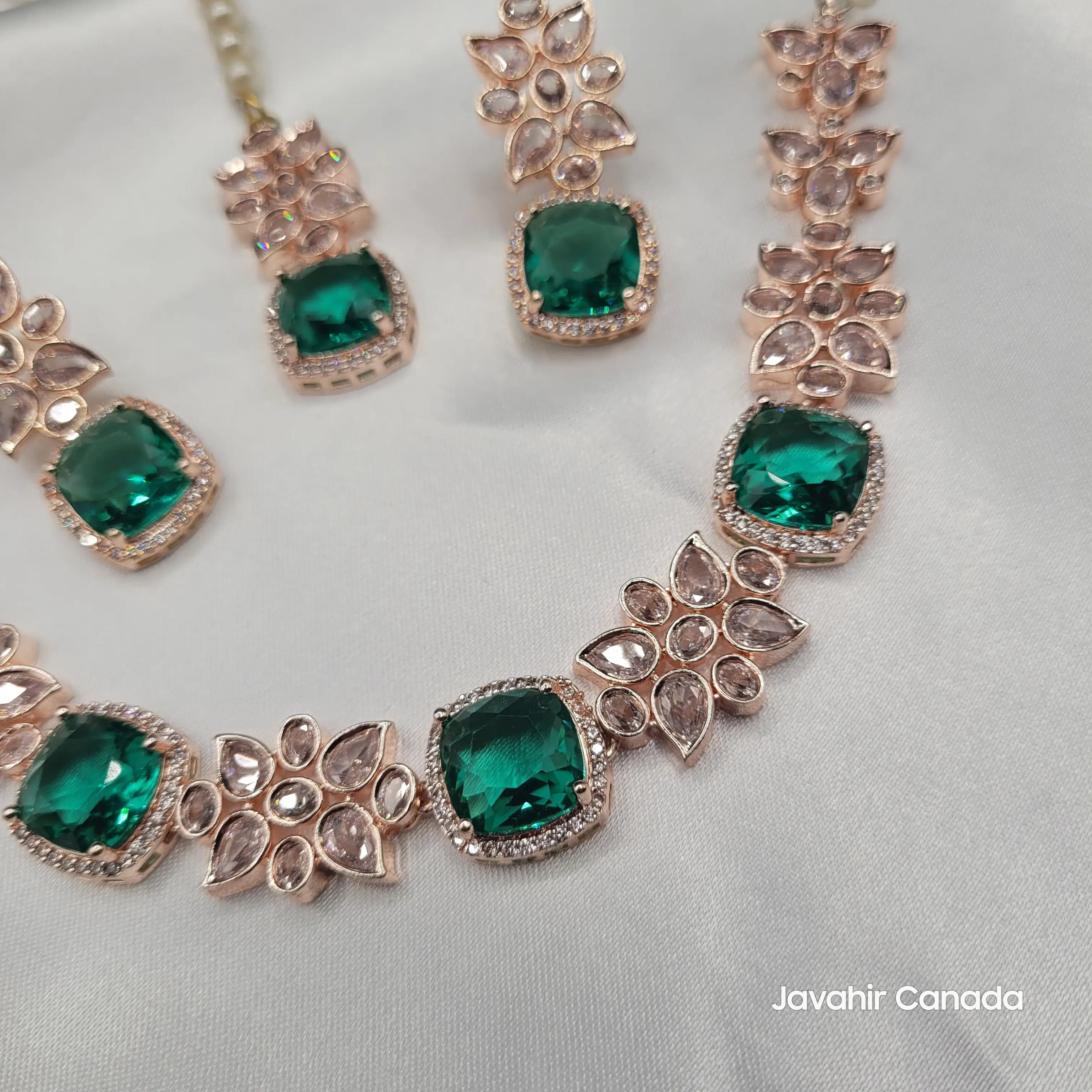 Jewelry set with emerald green gemstones and rose gold accents on a light gray background.