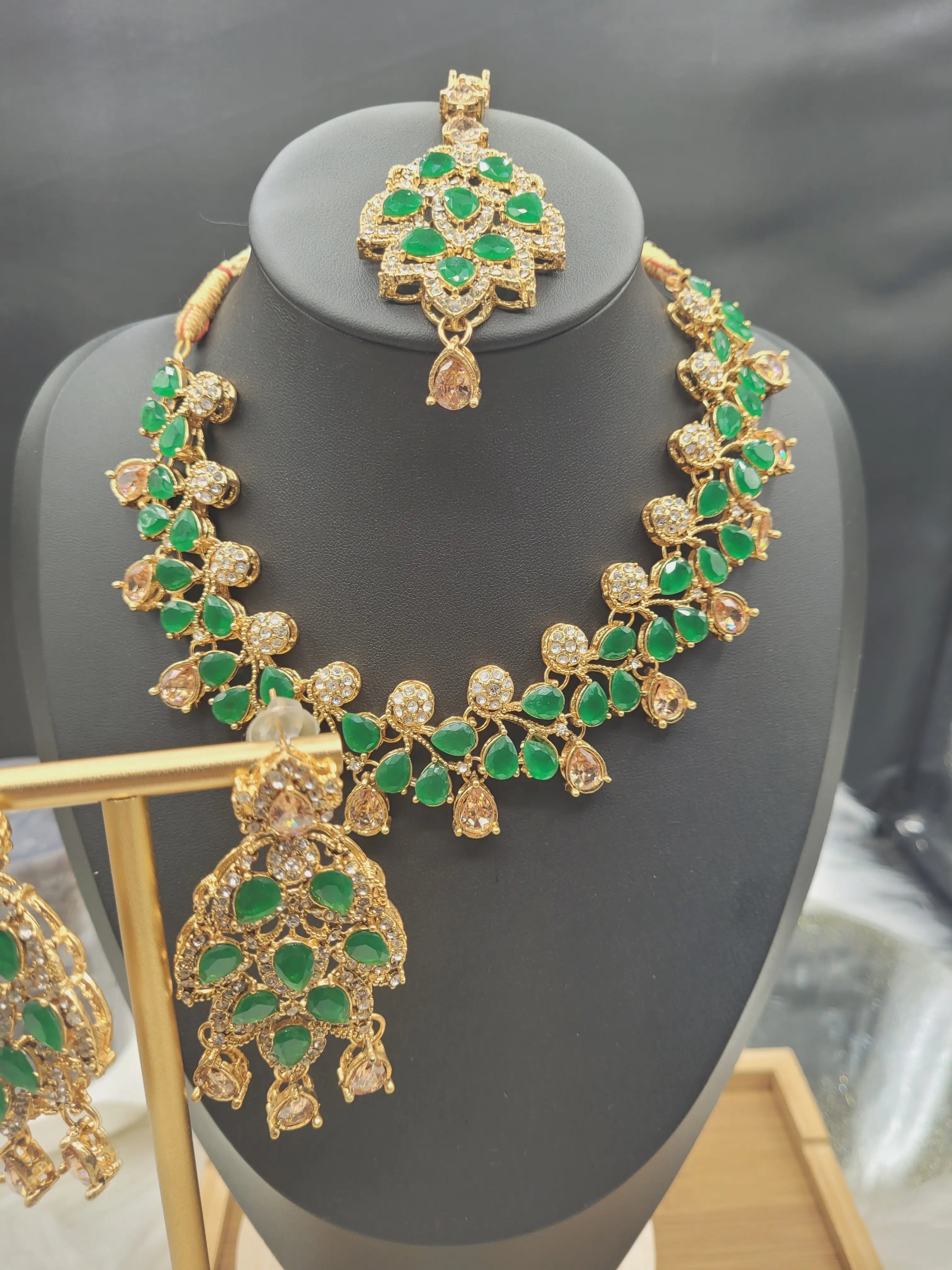 Full view of JV20 emerald necklace set with earrings and tikka on black stand 