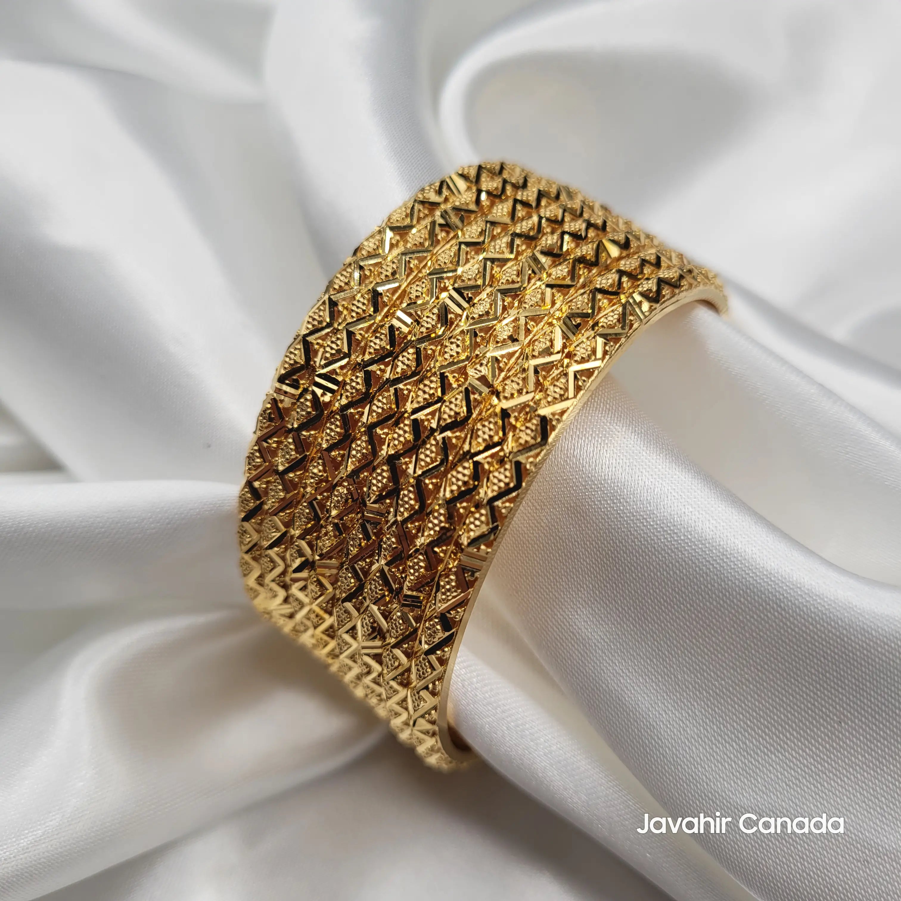 Wide diamond-pattern 22K gold plated bangles stacked on soft fabric
