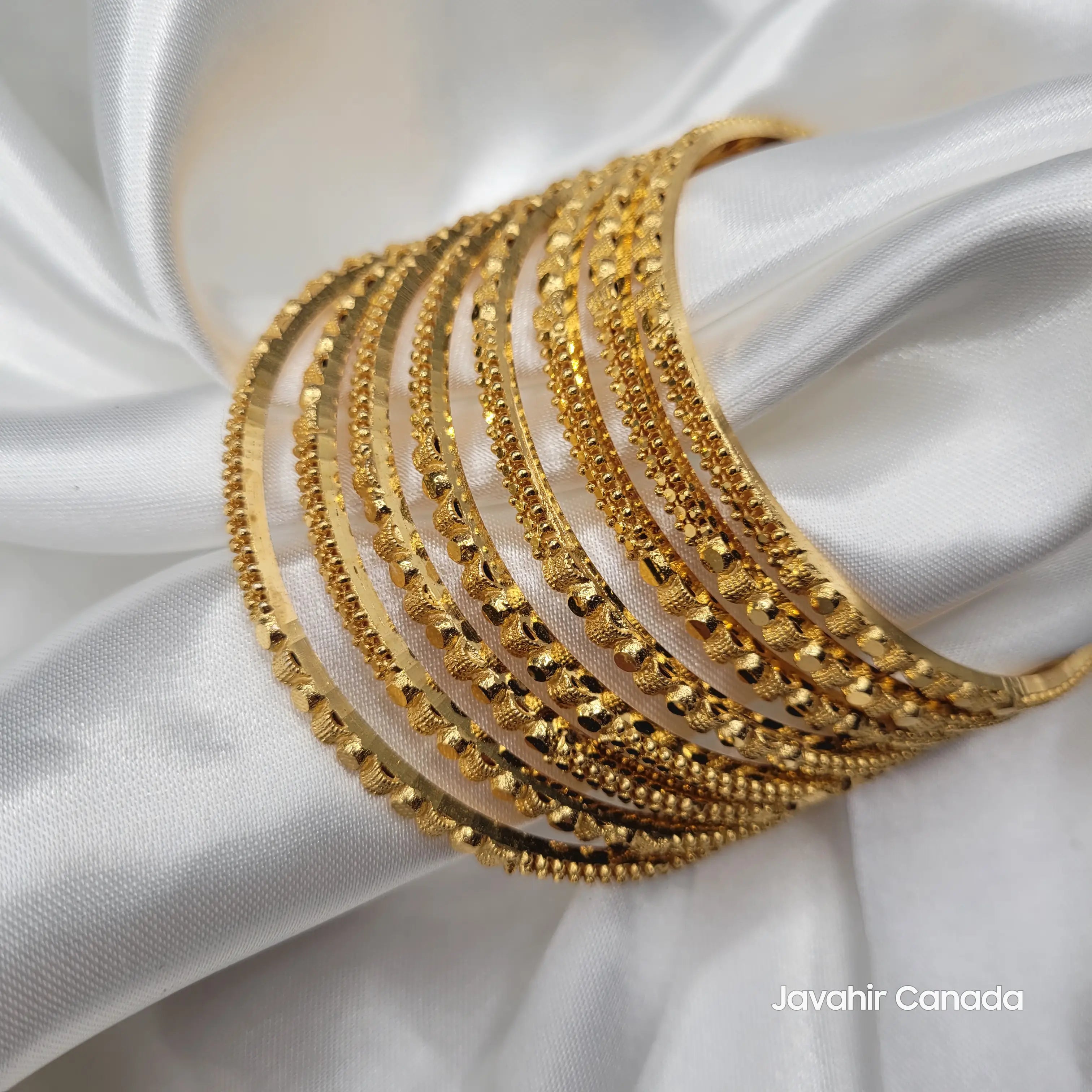 JV3034 set of 8 gold plated bangles with intricate texture on white satin