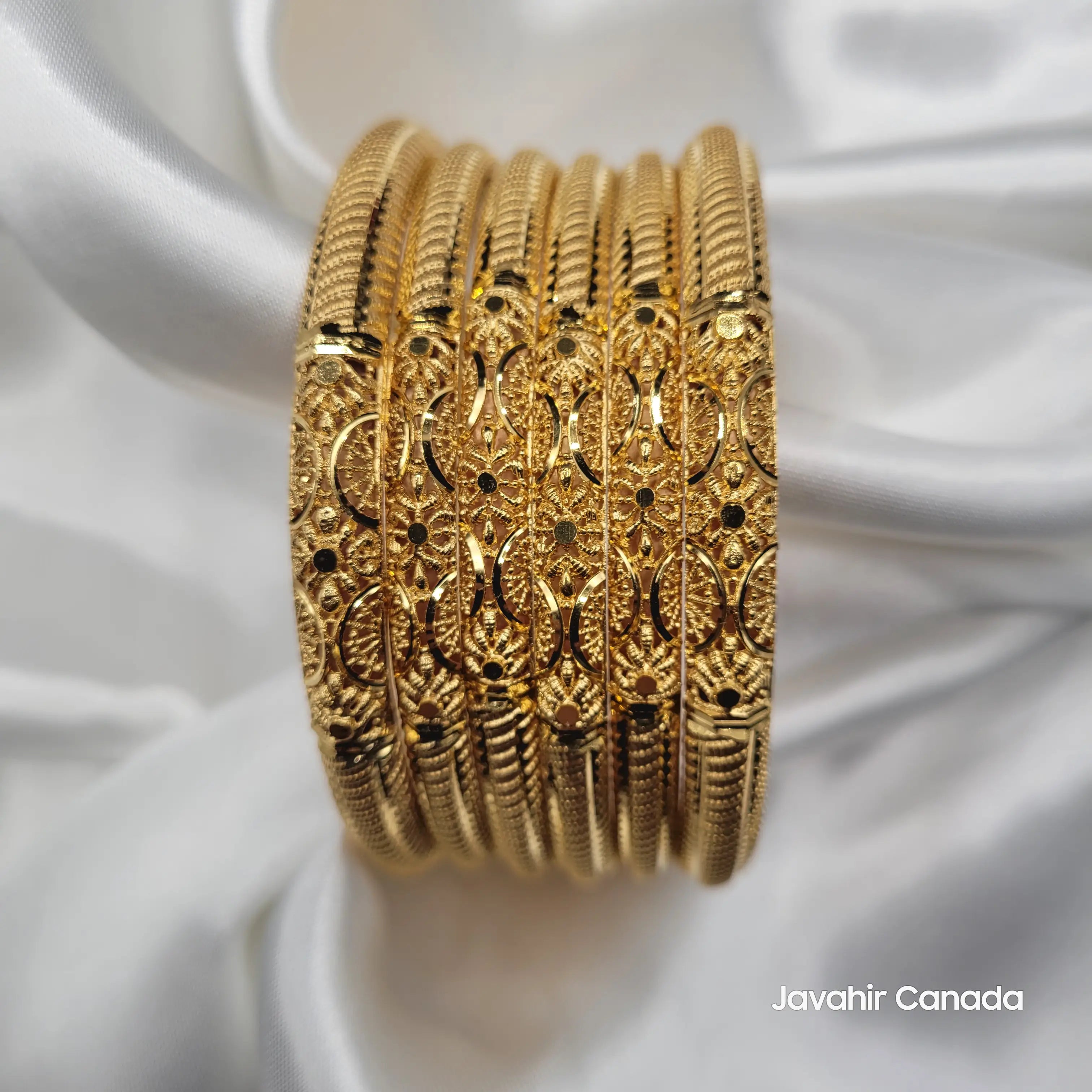 Six-piece gold bangles set arranged on white satin cloth