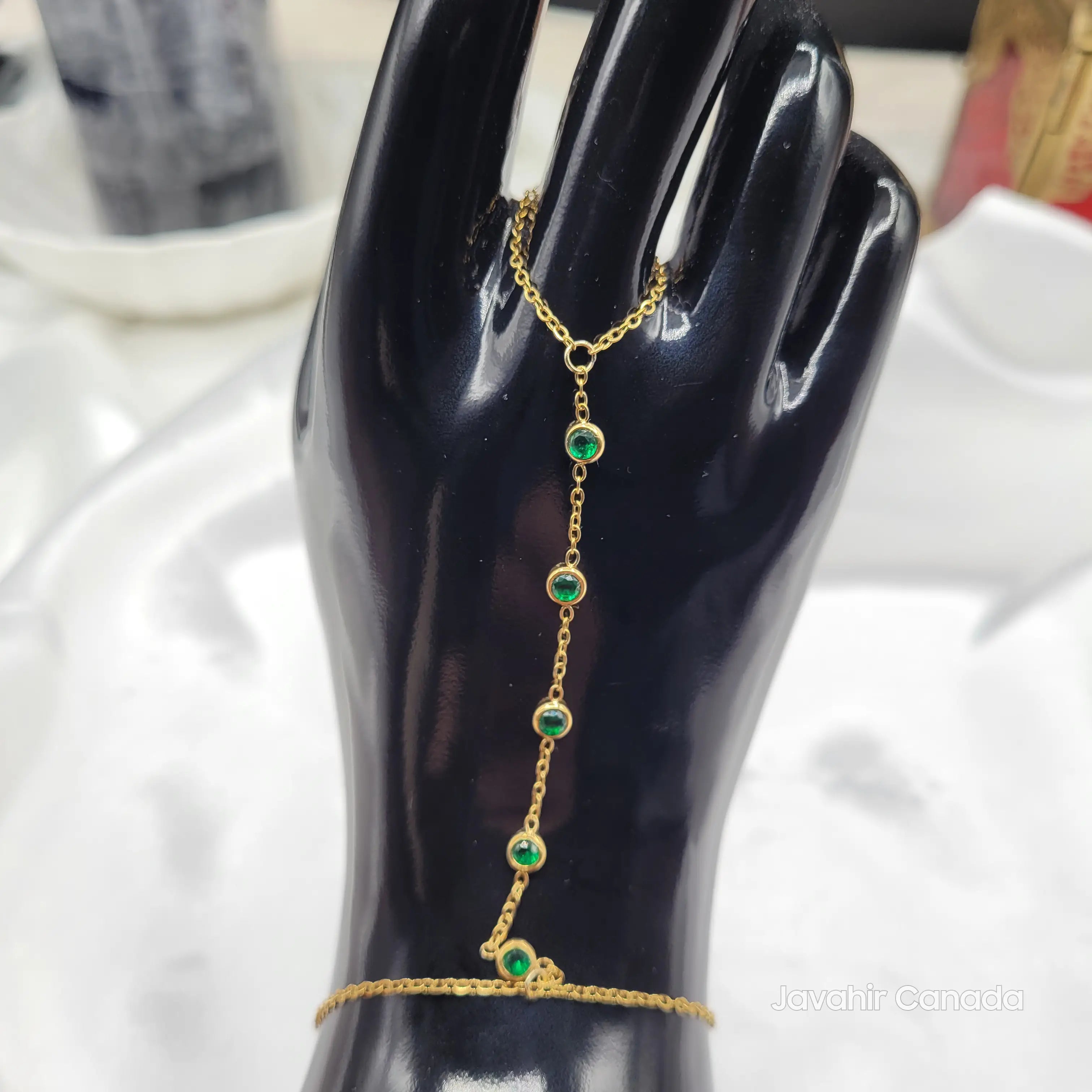 Gold chain bracelet with green gemstones on a black mannequin hand.