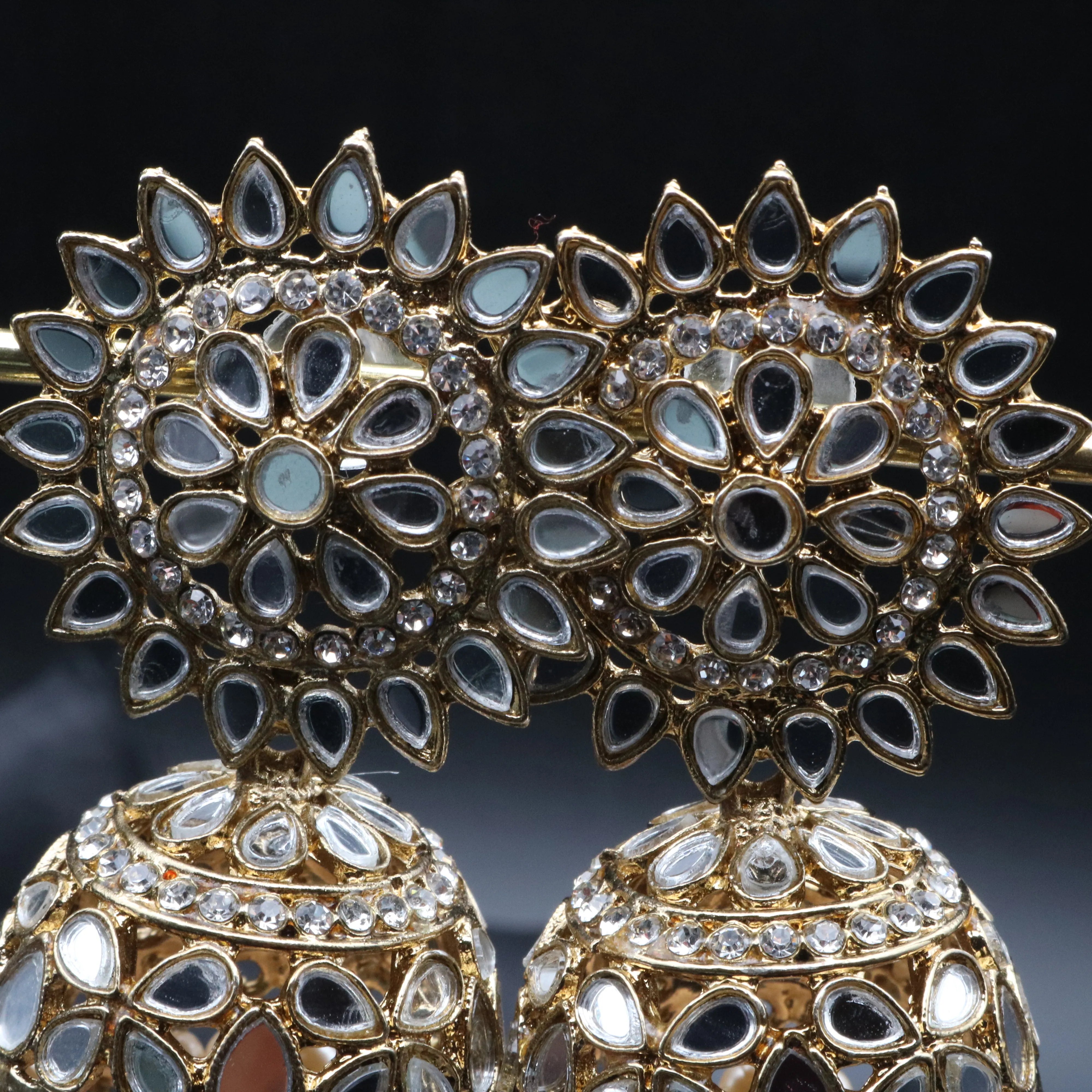 Pair of gold plated kundan jhumka earrings with a gray background