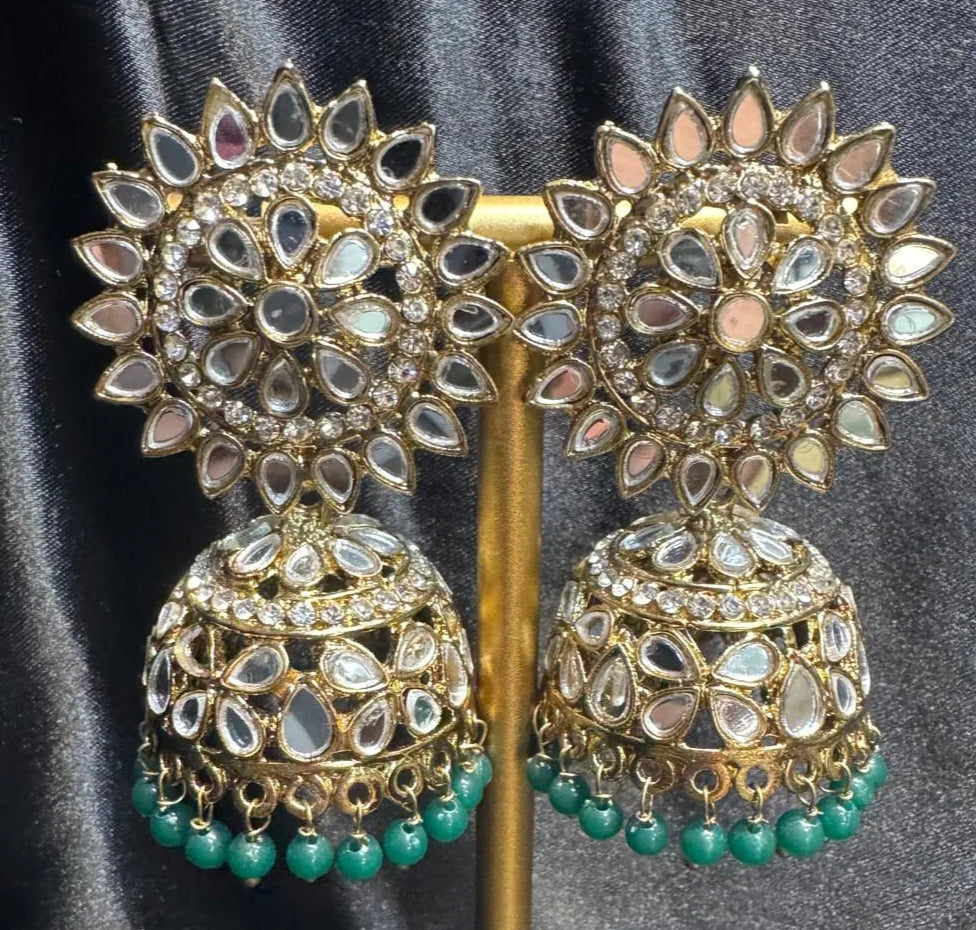 Pair of gold plated with green beads kundan jhumka earrings on a stand against a gray background