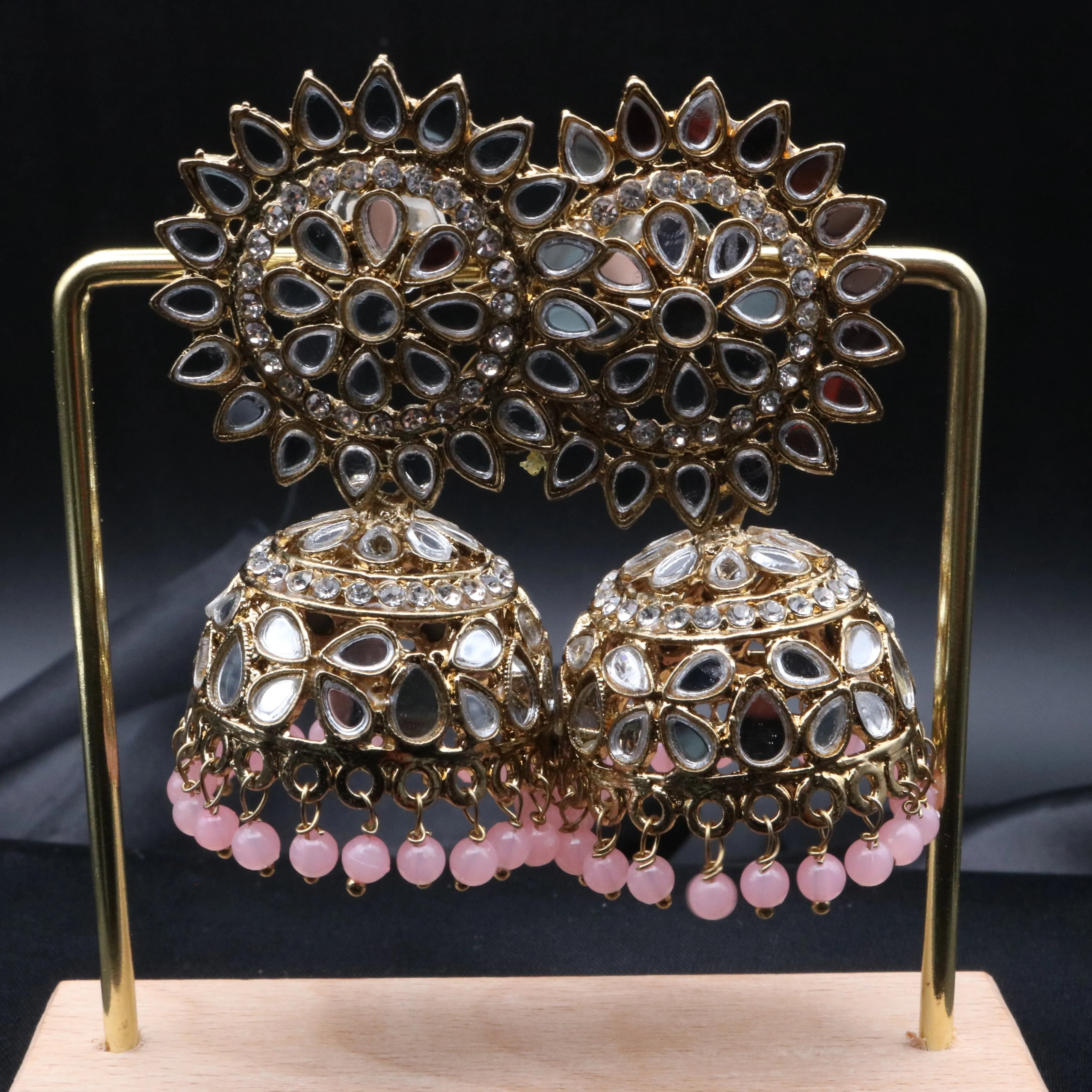 Pair of gold plated with light pink beads kundan jhumka earrings on a stand against a gray background