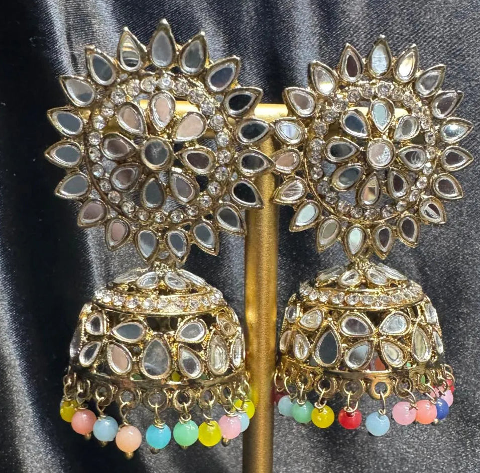 Pair of gold plated with colorful beads, kundan jhumka earrings on a stand against a gray background