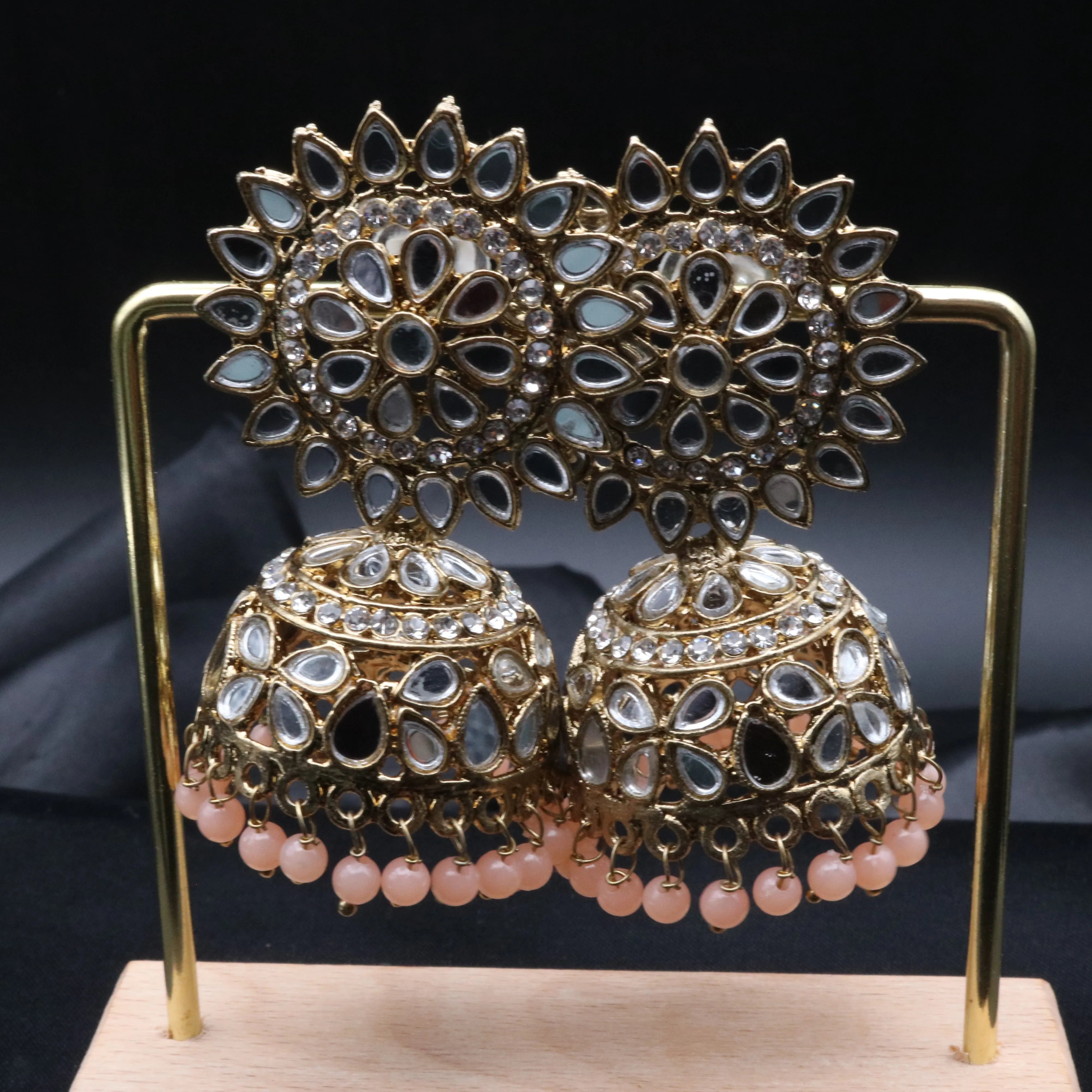 Pair of gold plated with peach beads kundan jhumka earrings on a stand against a gray background