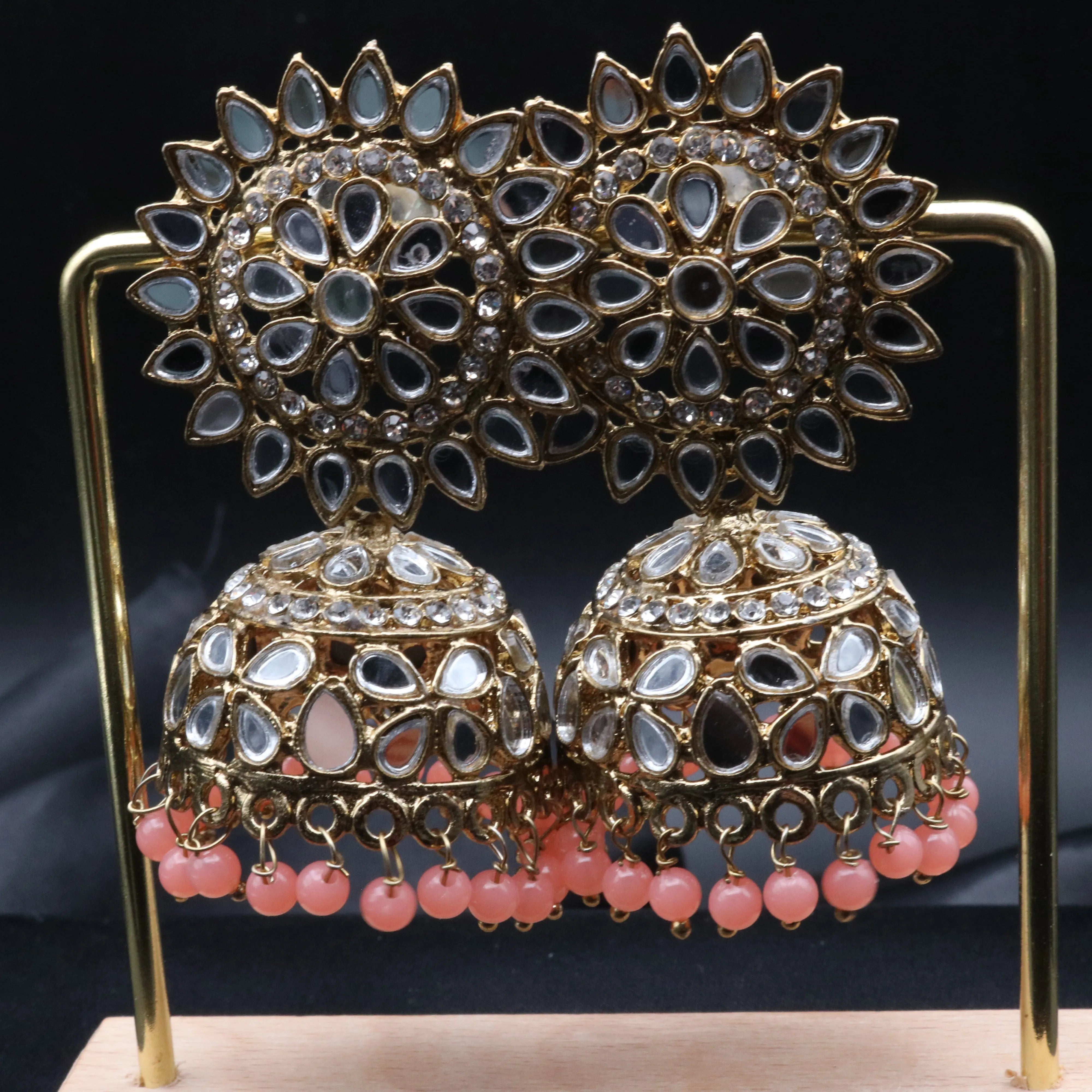 Pair of gold plated, with pink beads, kundan jhumka earrings on a stand against a gray background