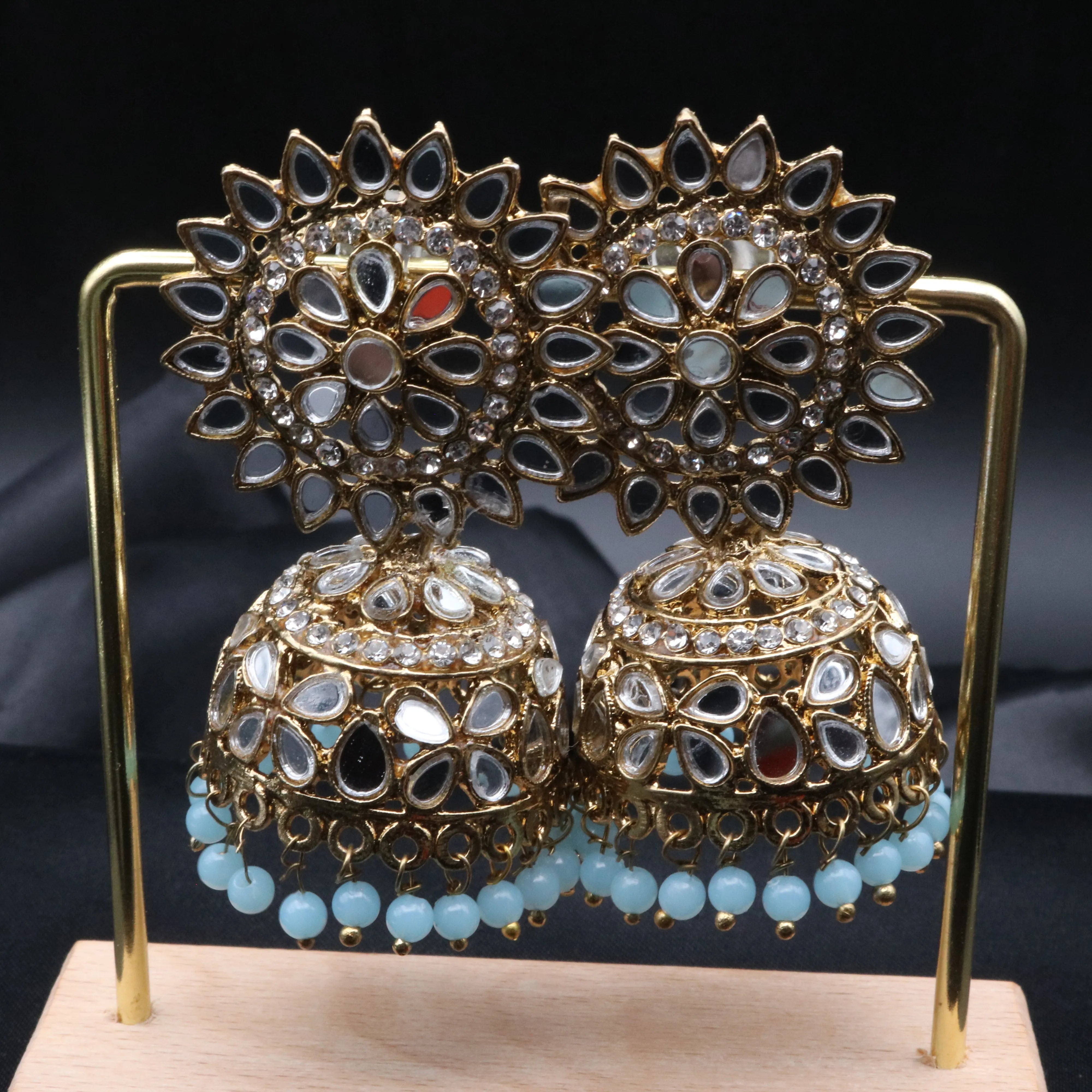 Pair of gold plated with teal beads kundan jhumka earrings on a stand against a gray background