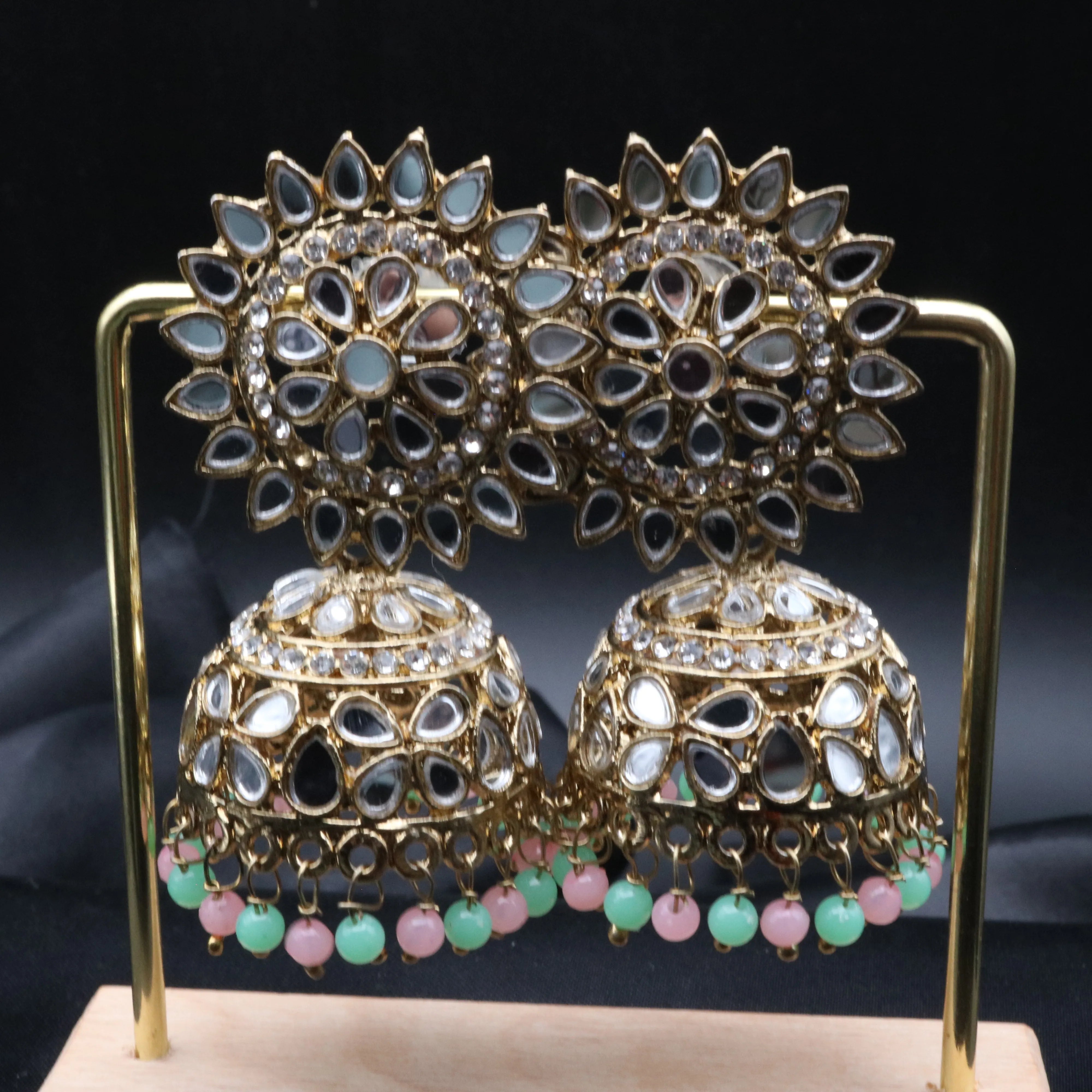 Pair of gold plated, with teal and pink beads, kundan jhumka earrings on a stand against a gray background