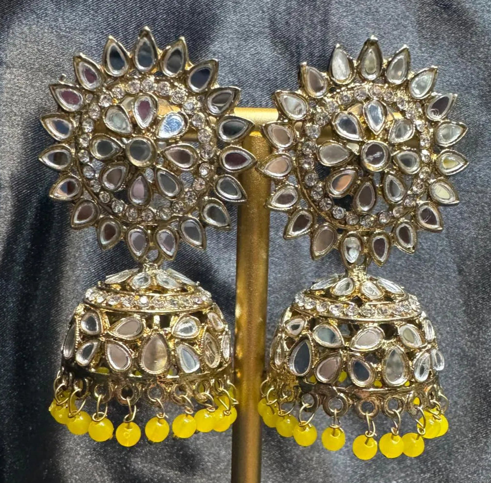 Pair of gold plated and yellow kundan jhumka earrings on a stand against a gray background