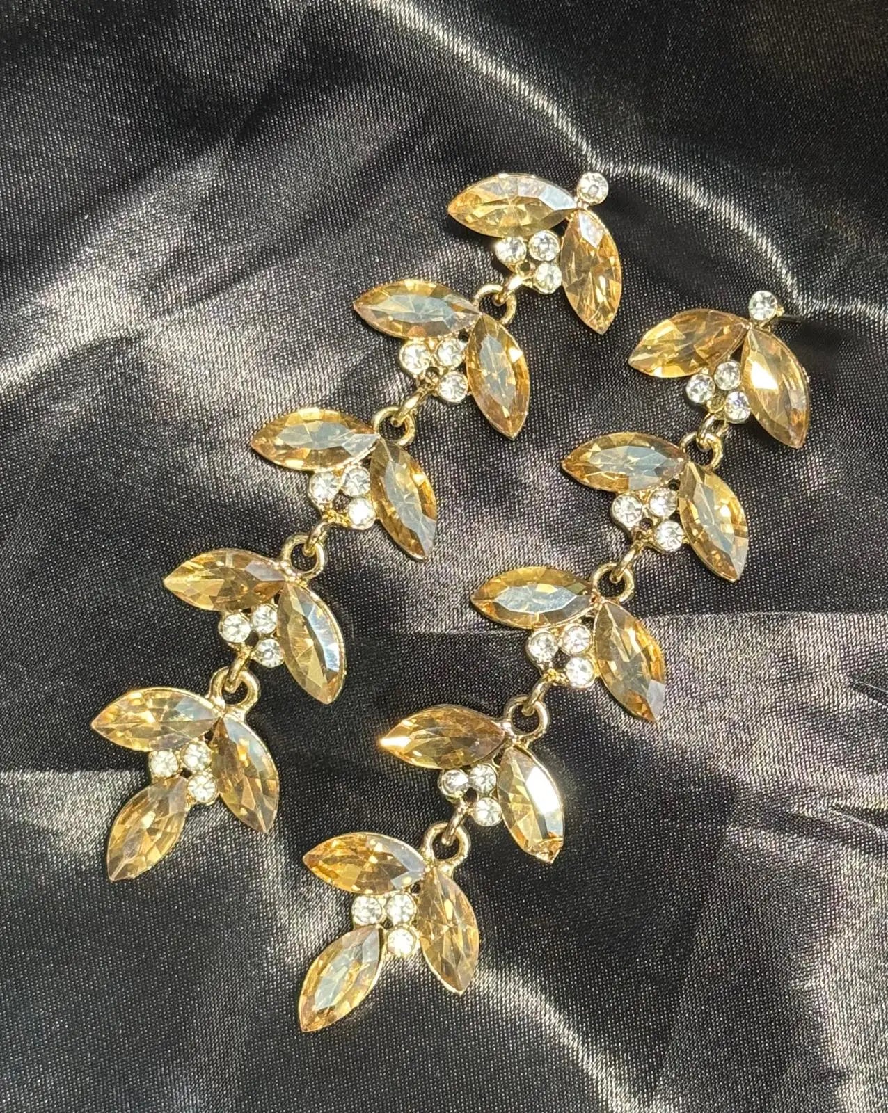 Another view of gold-plated leaf-shaped earrings with clear stones on a dark fabric background. Handcrafted in Pakistan