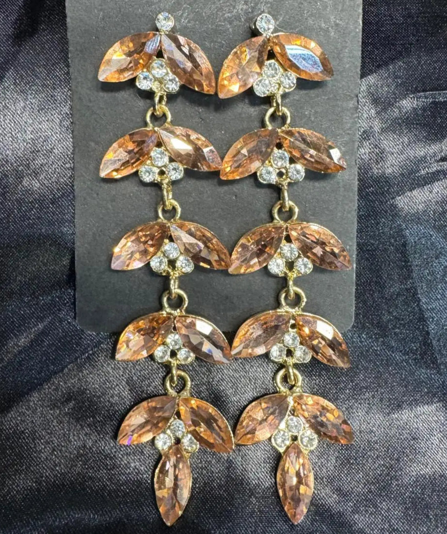 another view of gold-plated leaf-shaped earrings with clear pink stones on a dark fabric background. Handcrafted in Pakistan