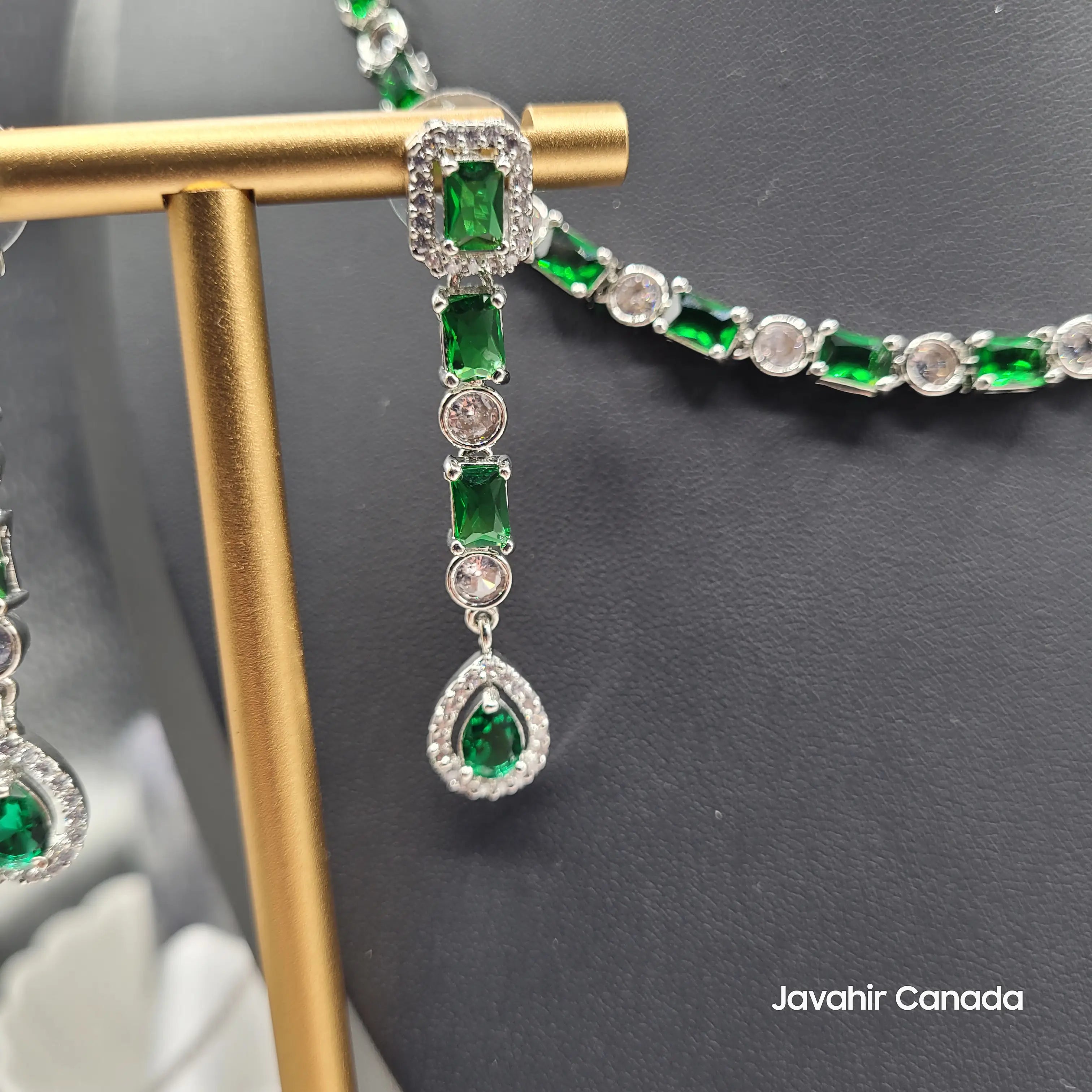 Close-up of Luna earrings featuring emerald-cut green CZ stones and pear-drop dangle design.