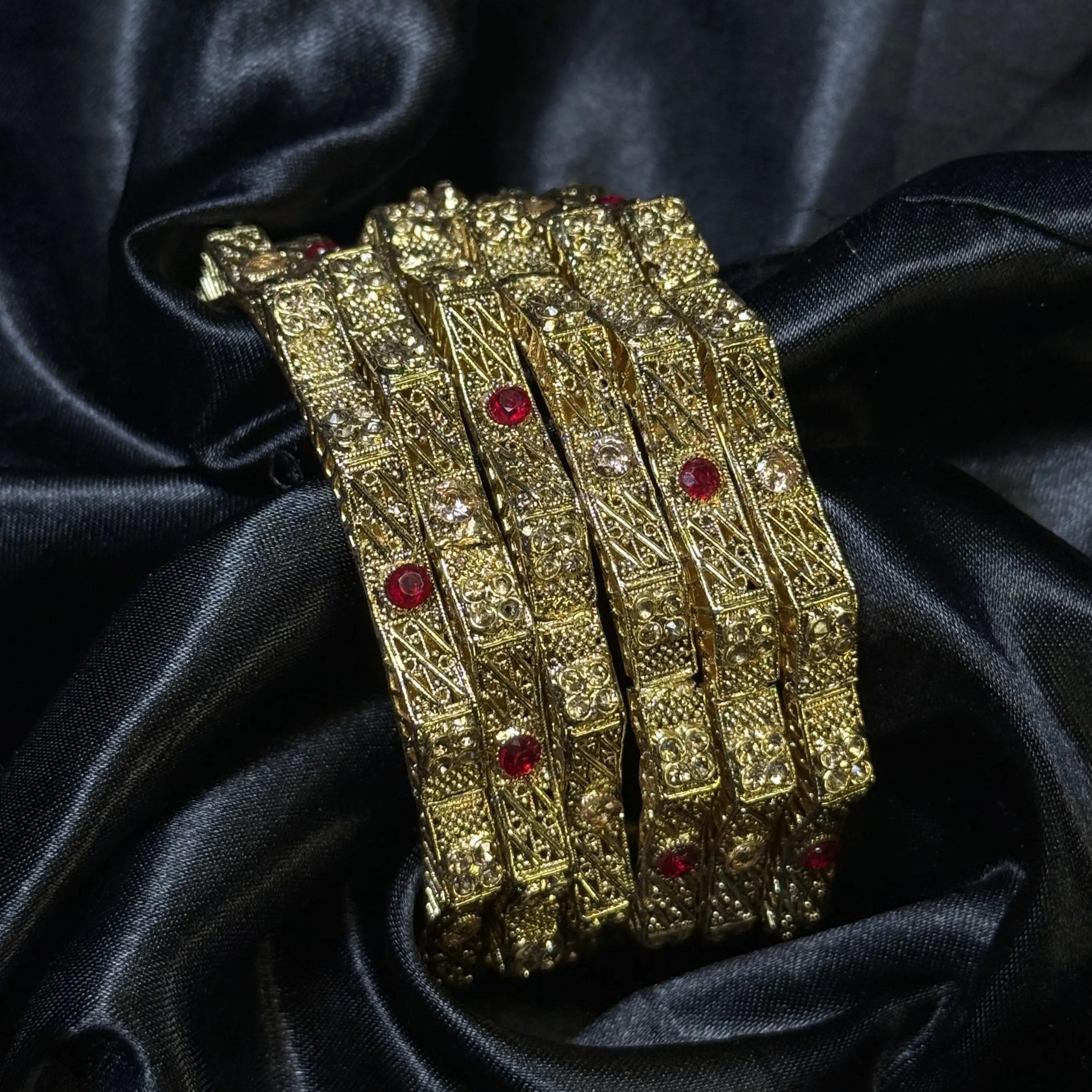 Traditional gold bangles with red crystal stones on black fabric