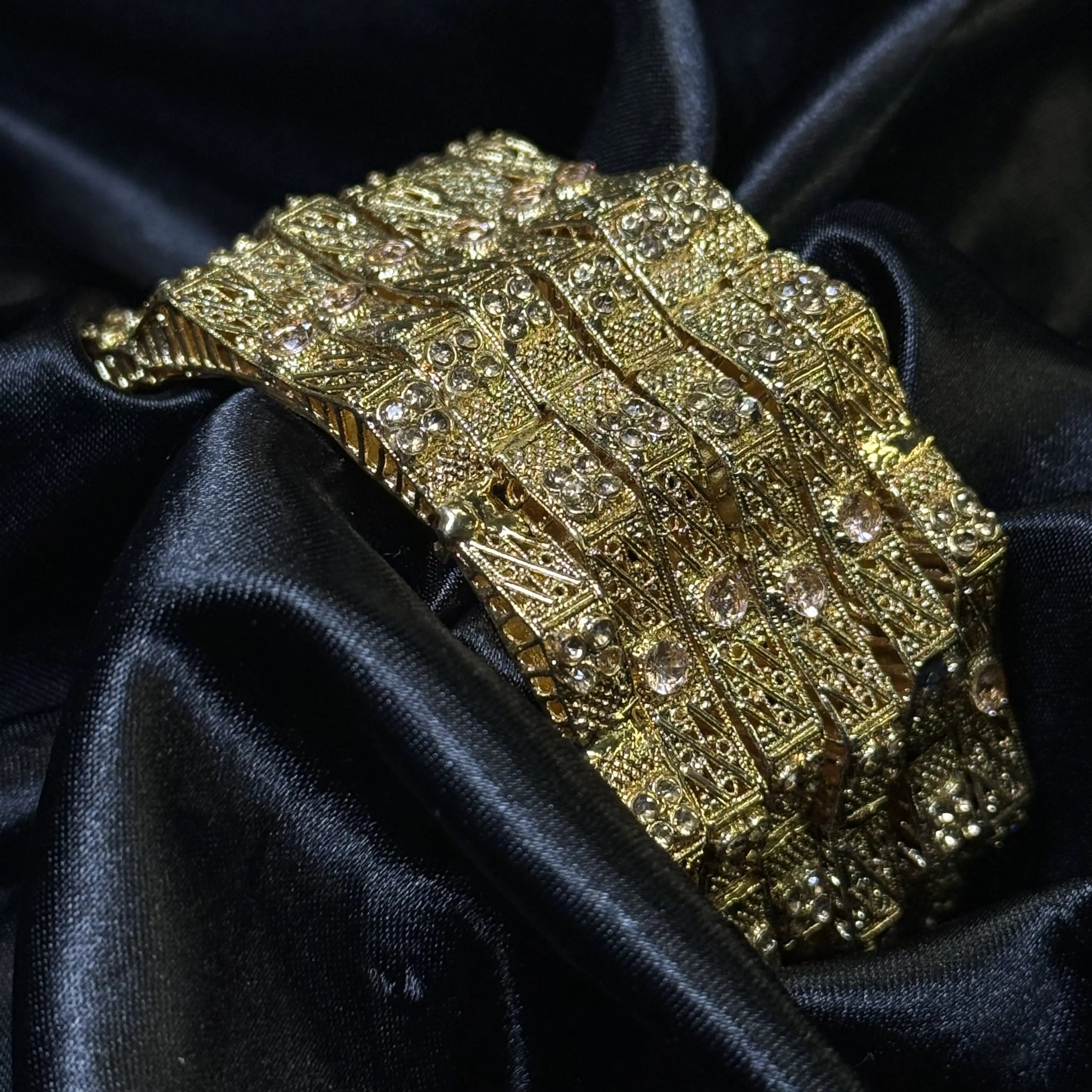 Gold bangle set with clear stones and filigree design on black satin