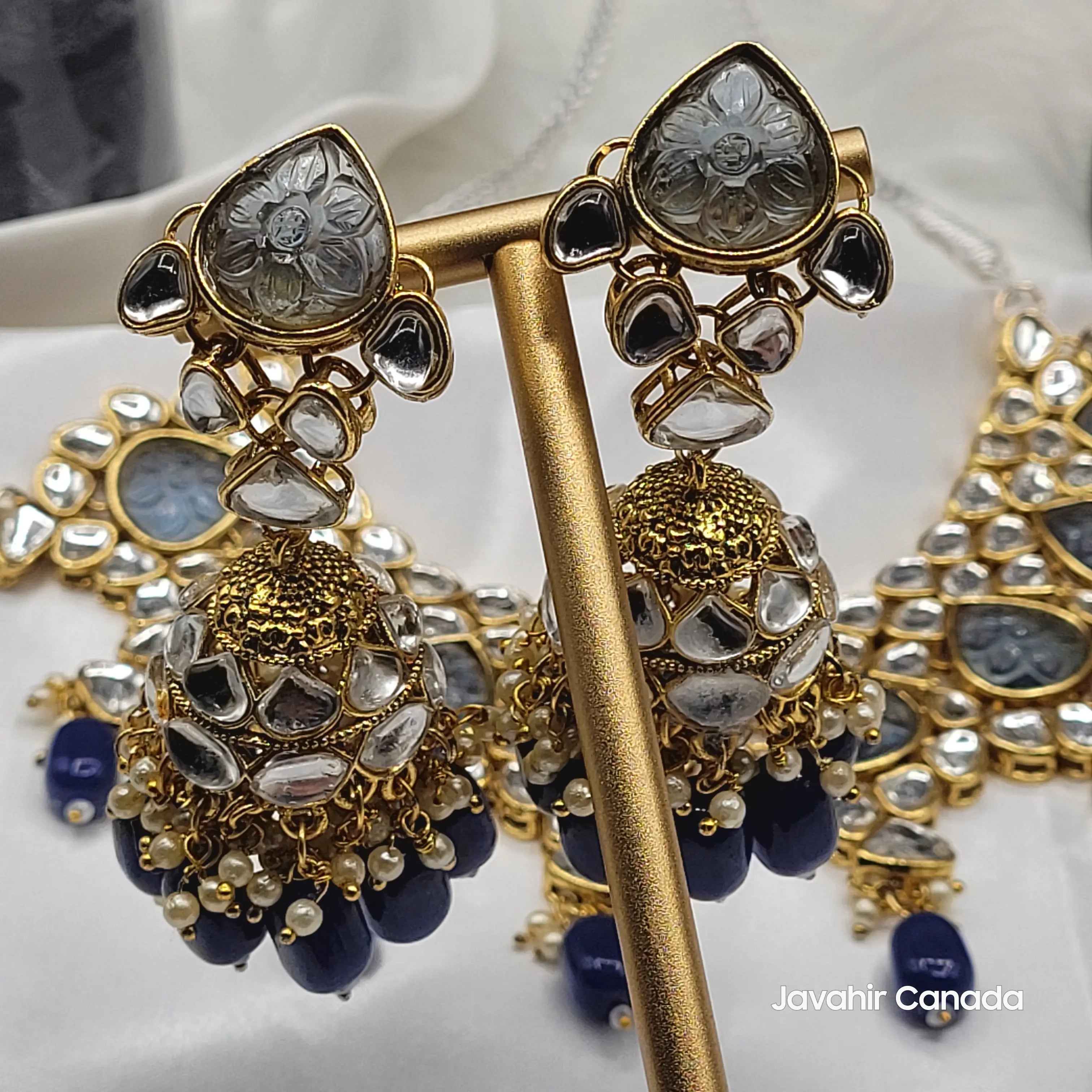 Close-up of Marina jhumka earrings with carved glass tops, kundan detailing, and navy blue bead drops on gold base.