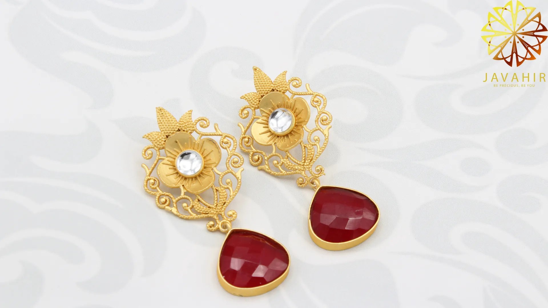 Gold plated earrings with red stones on a white background, featuring the Javahir brand.