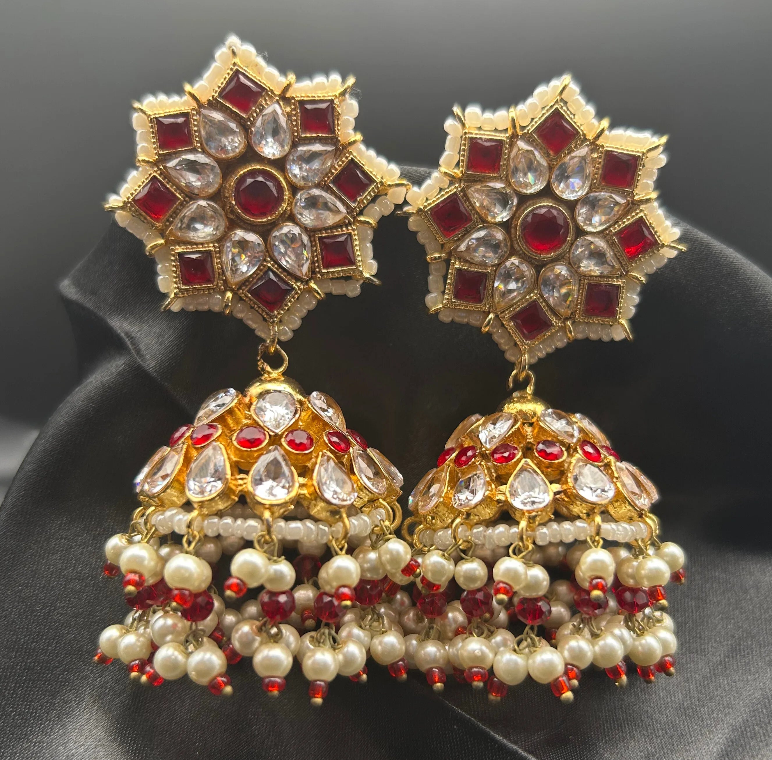 Ornate gold, red, and pearl earrings on a dark fabric background