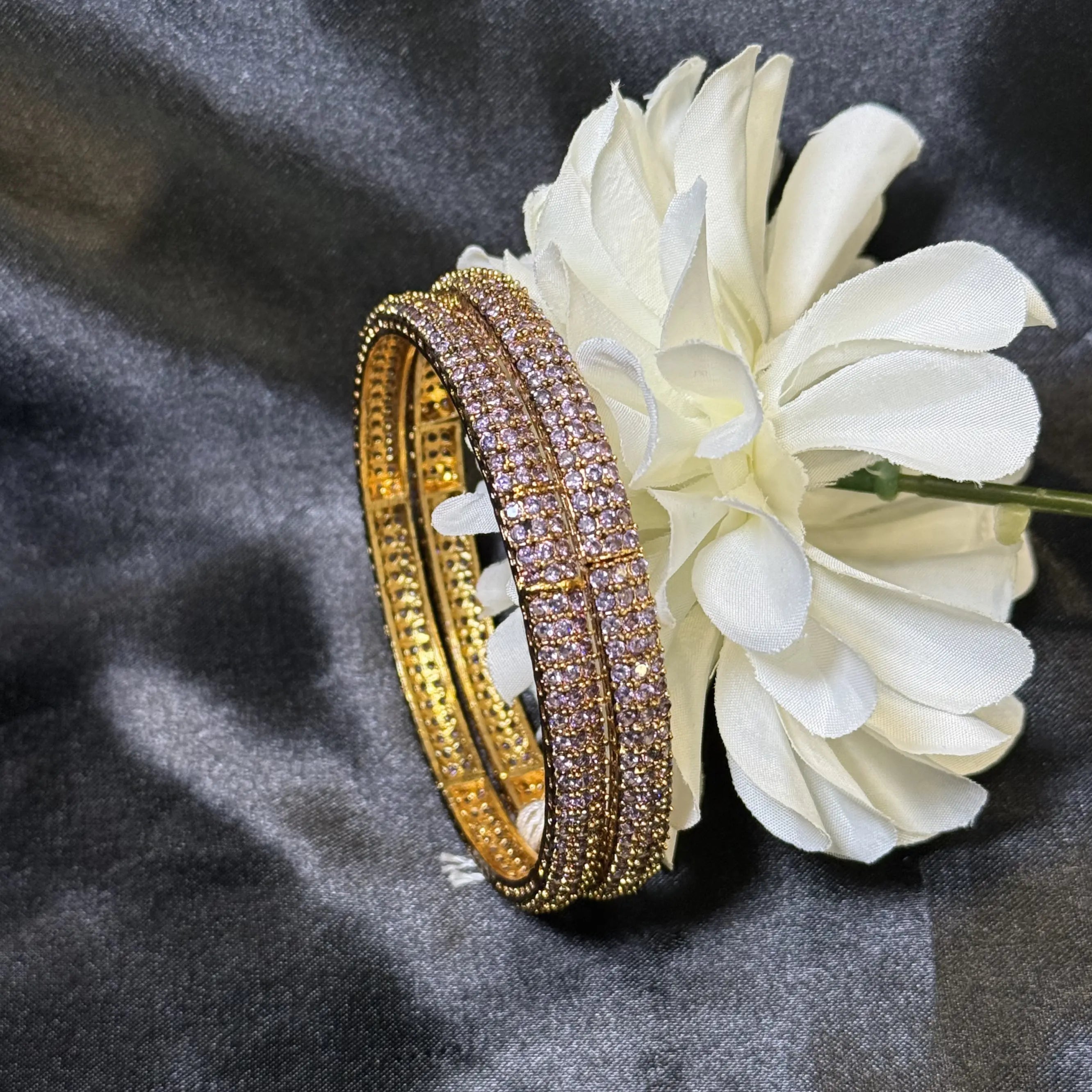 Gold bangles with purple gemstones on a white flower against a dark gray background