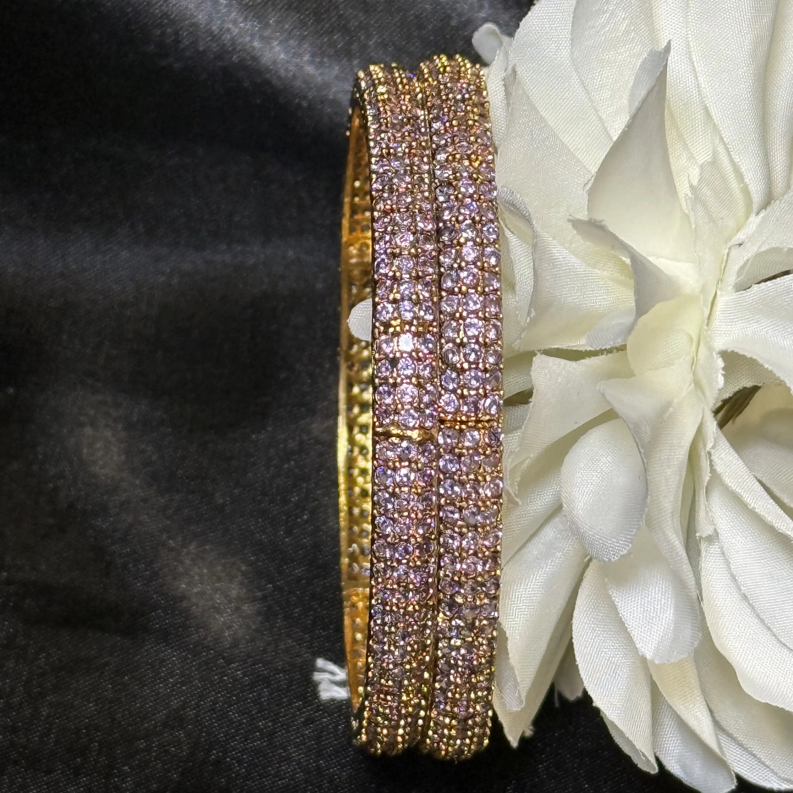 Gold bangles with purple gemstones on a white flower against a black background