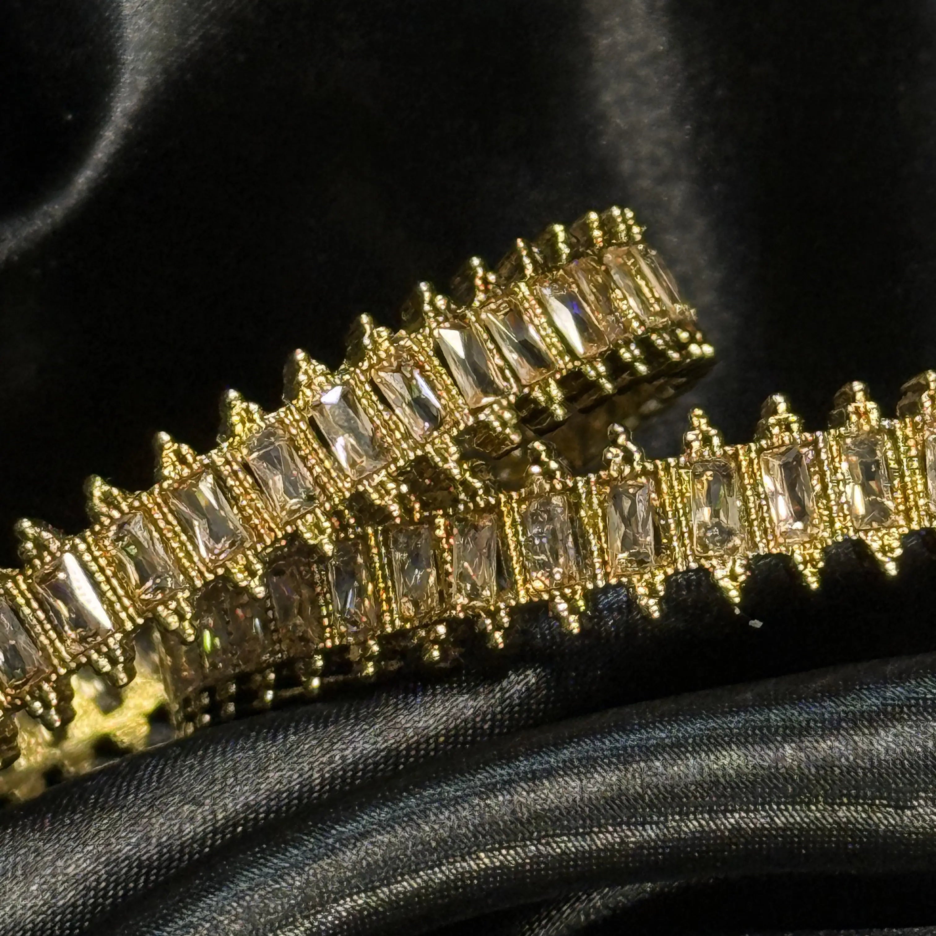 Gold bracelet with clear stones on a black satin background