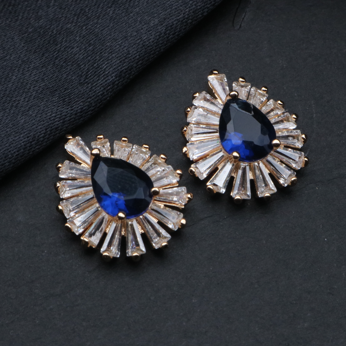 A pair of NEBULA earrings featuring a stainless steel and gold plated design with blue stones and clear accent stones.
