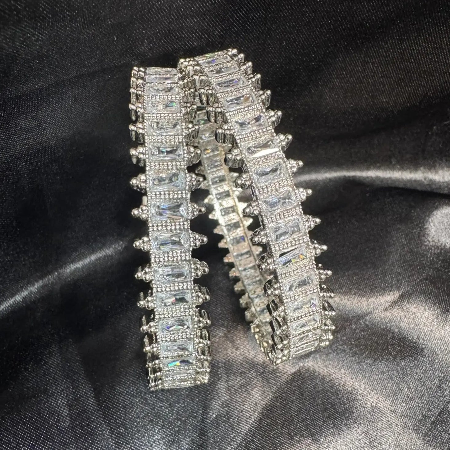 Pair of silver American diamond bangles on a black satin background