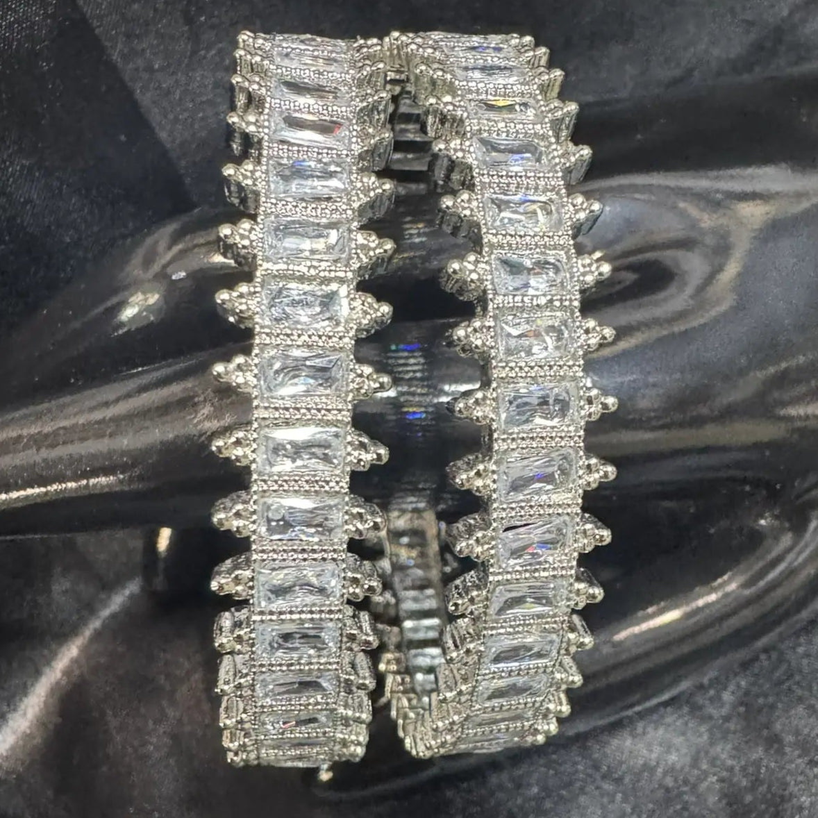 Silver bangles with clear gemstones on a dark, textured fabric background
