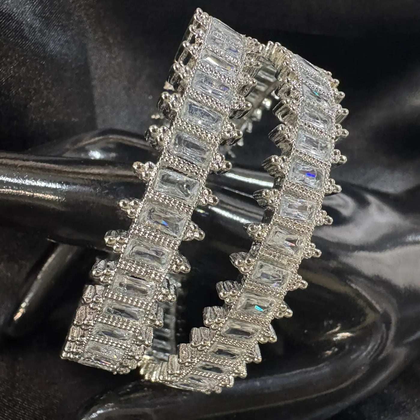 Silver bangles with baguette-cut gemstones on a dark fabric background