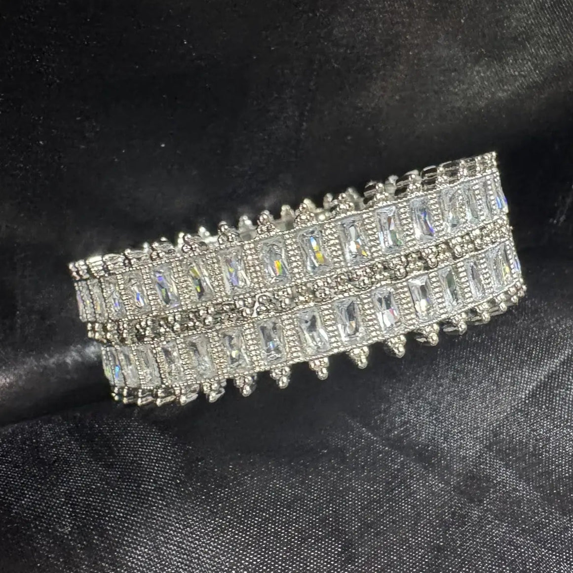 Silver bangles with clear gemstones on a black fabric background