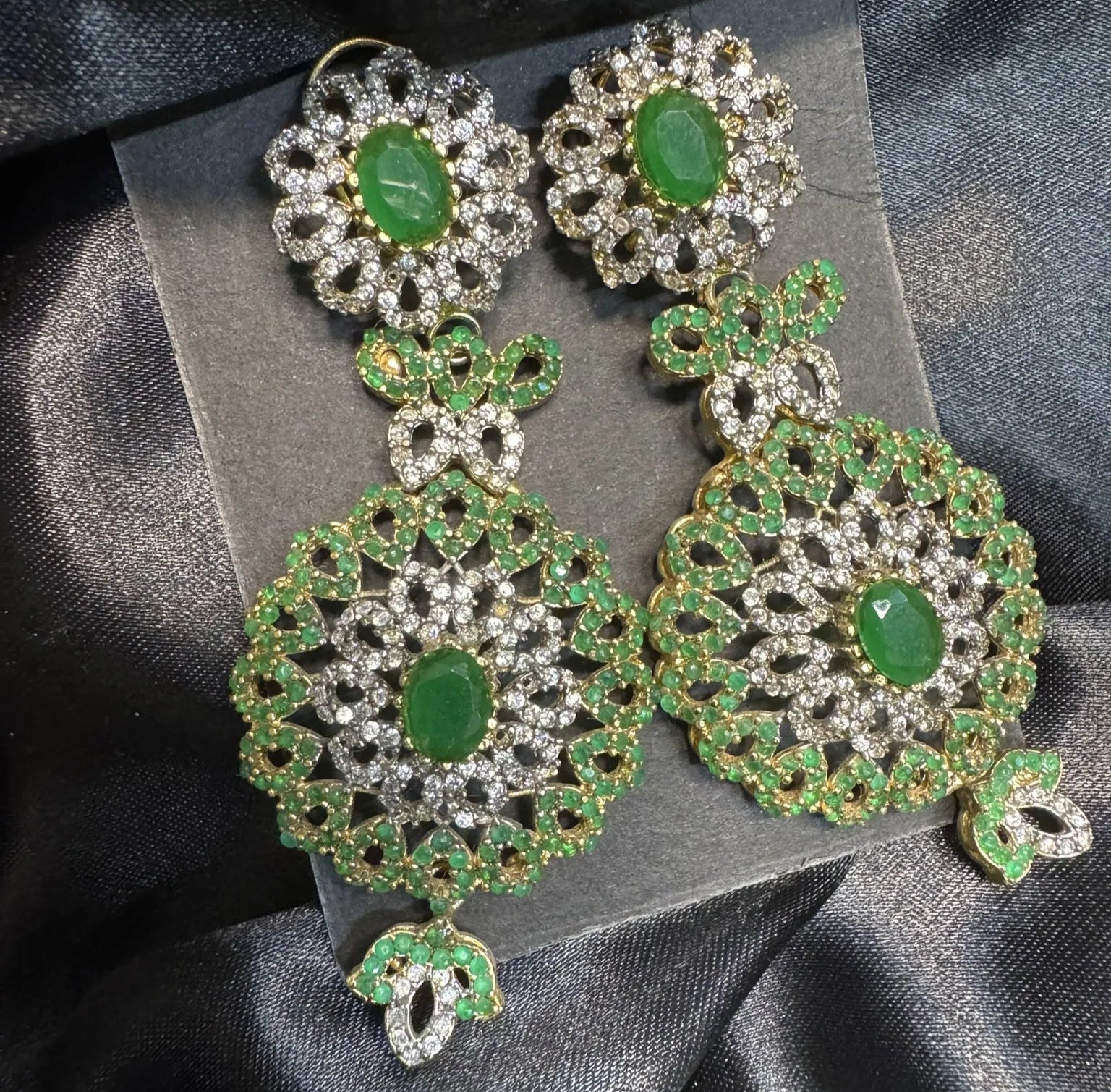 Ornate green and silver earrings on a black satin background
